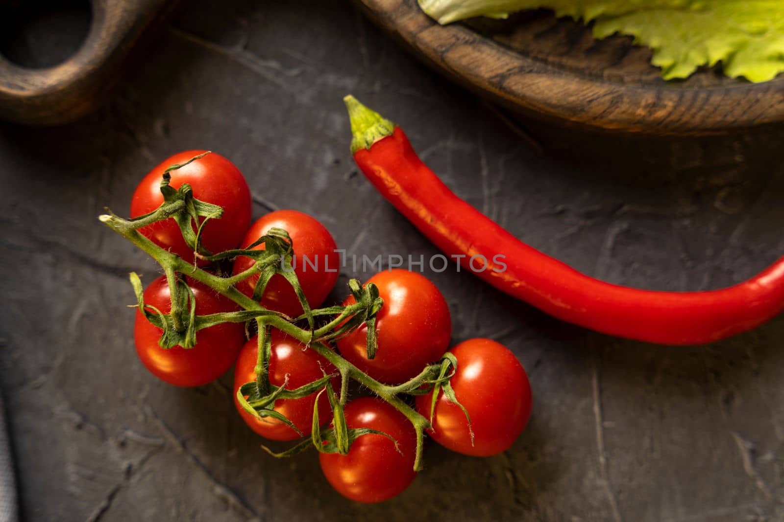 Delicious ripe cherry tomatoes, chili peppers and garlic for cooking on a dark background. Top view.