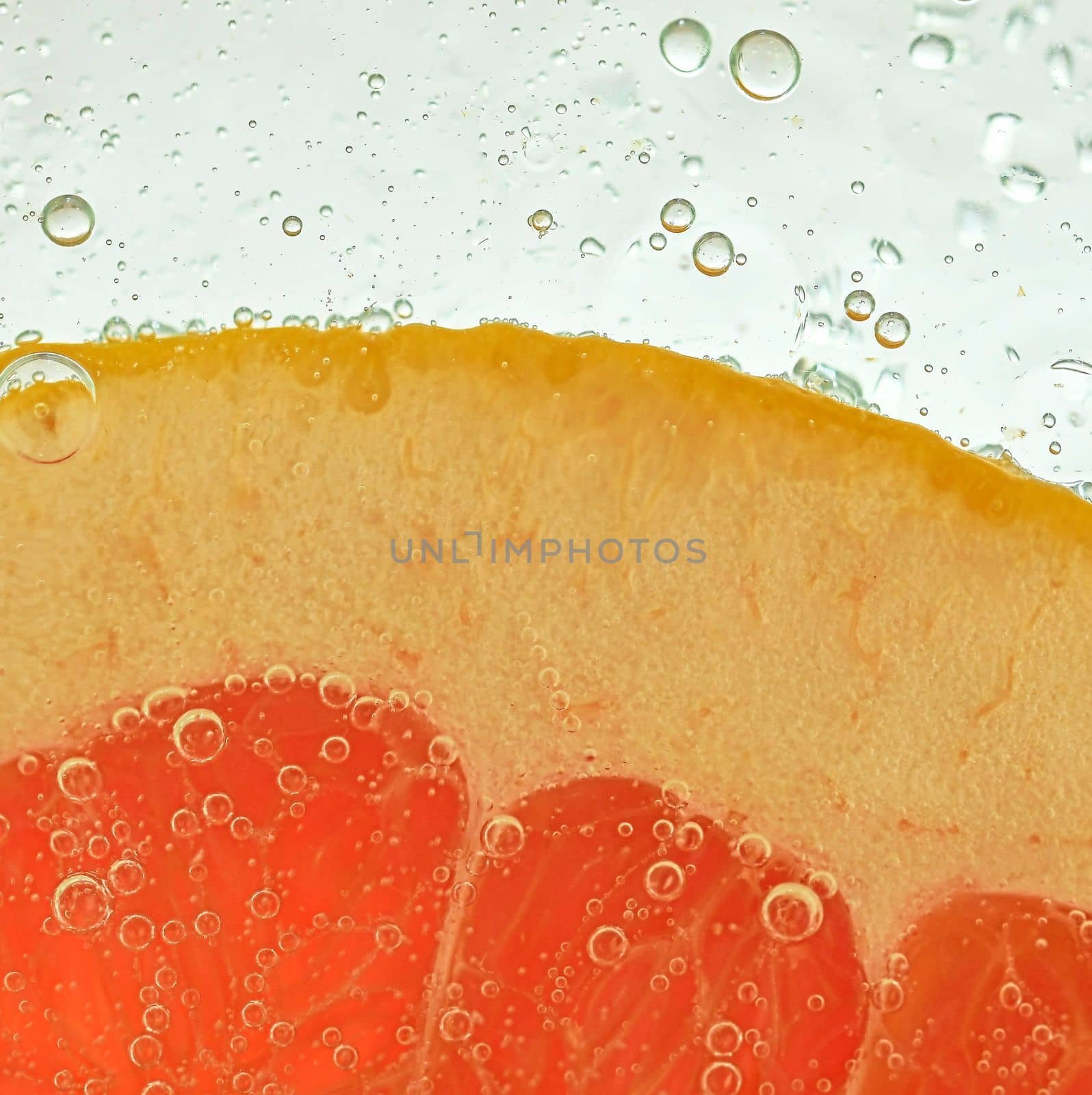 Slice of red grapefruit in water on white background. Grapefruit close-up in liquid with bubbles. Slice of red ripe grapefruit in water. Macro image of fruit in water.