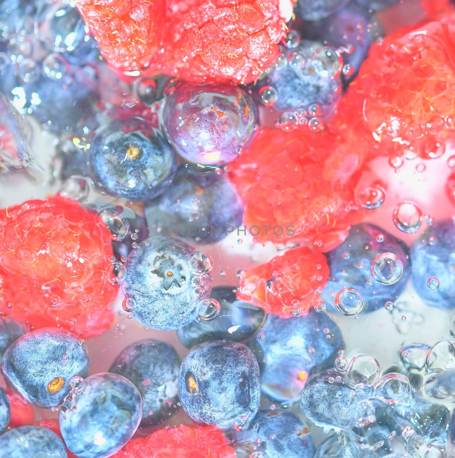 Water with fresh berries, close-up. Close-up view of the blueberries and raspberries in water background. Texture of bilberries and raspberries with macro bubbles on the glass wall. Flat design, top view. Horizontal image. Defocused by roman_nerud