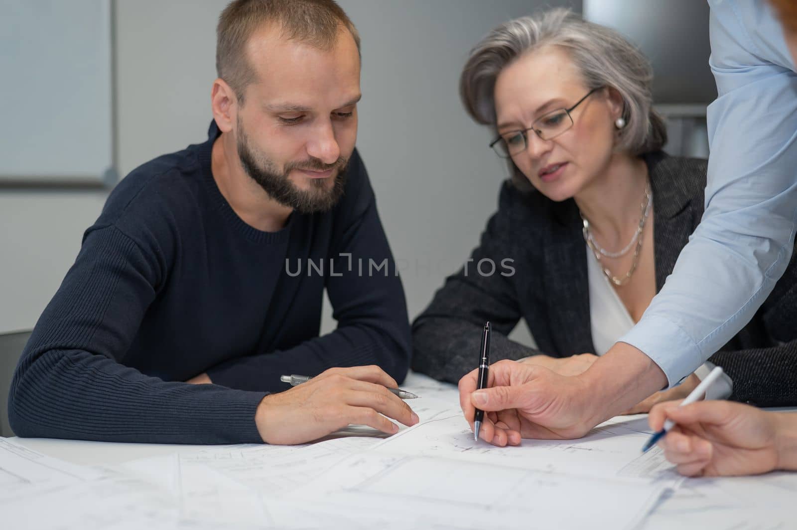 Four colleagues are discussing blueprints in a conference room in an office. Brainstorming of engineers and architects