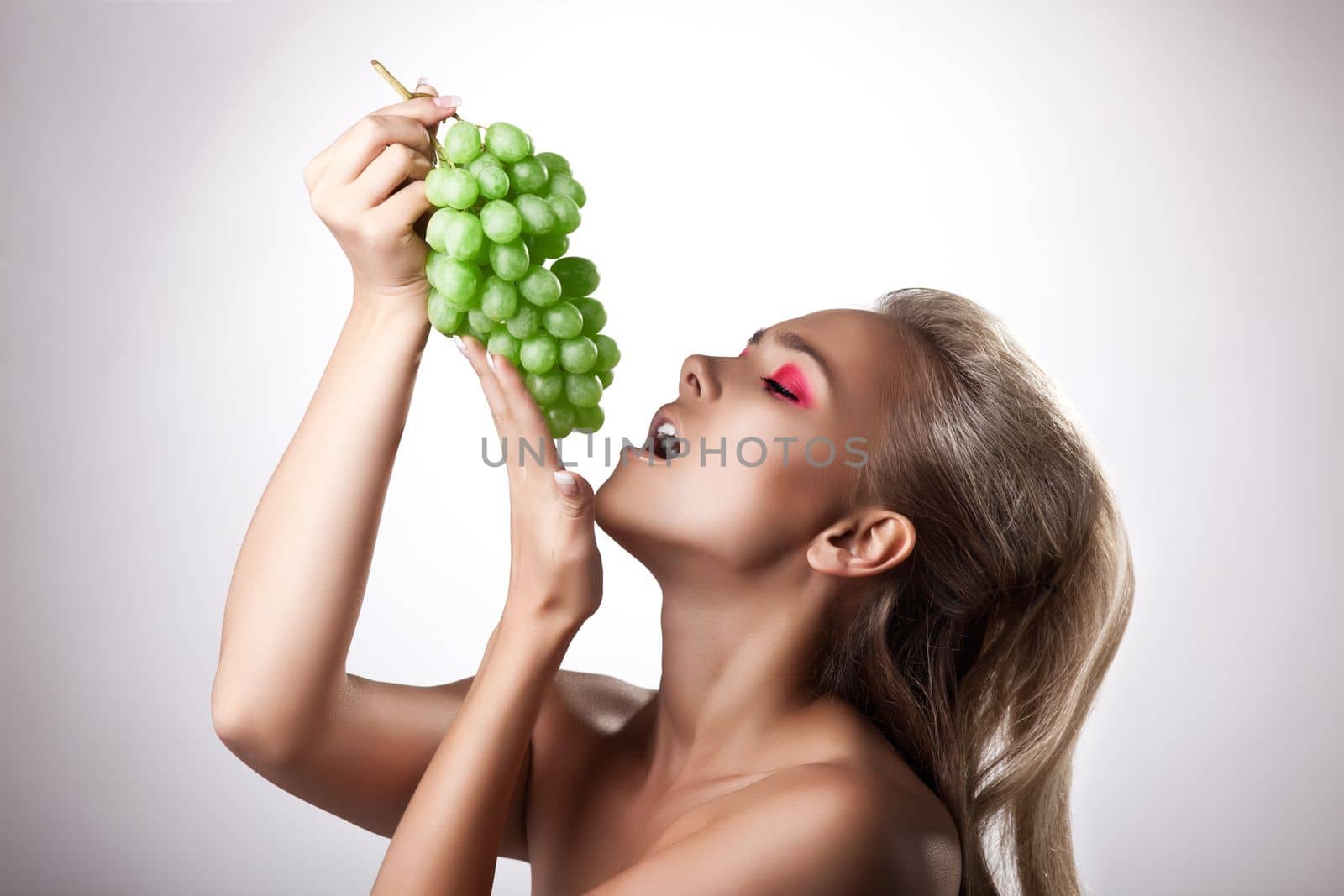 Sexy young woman eat green grapes studio portrait