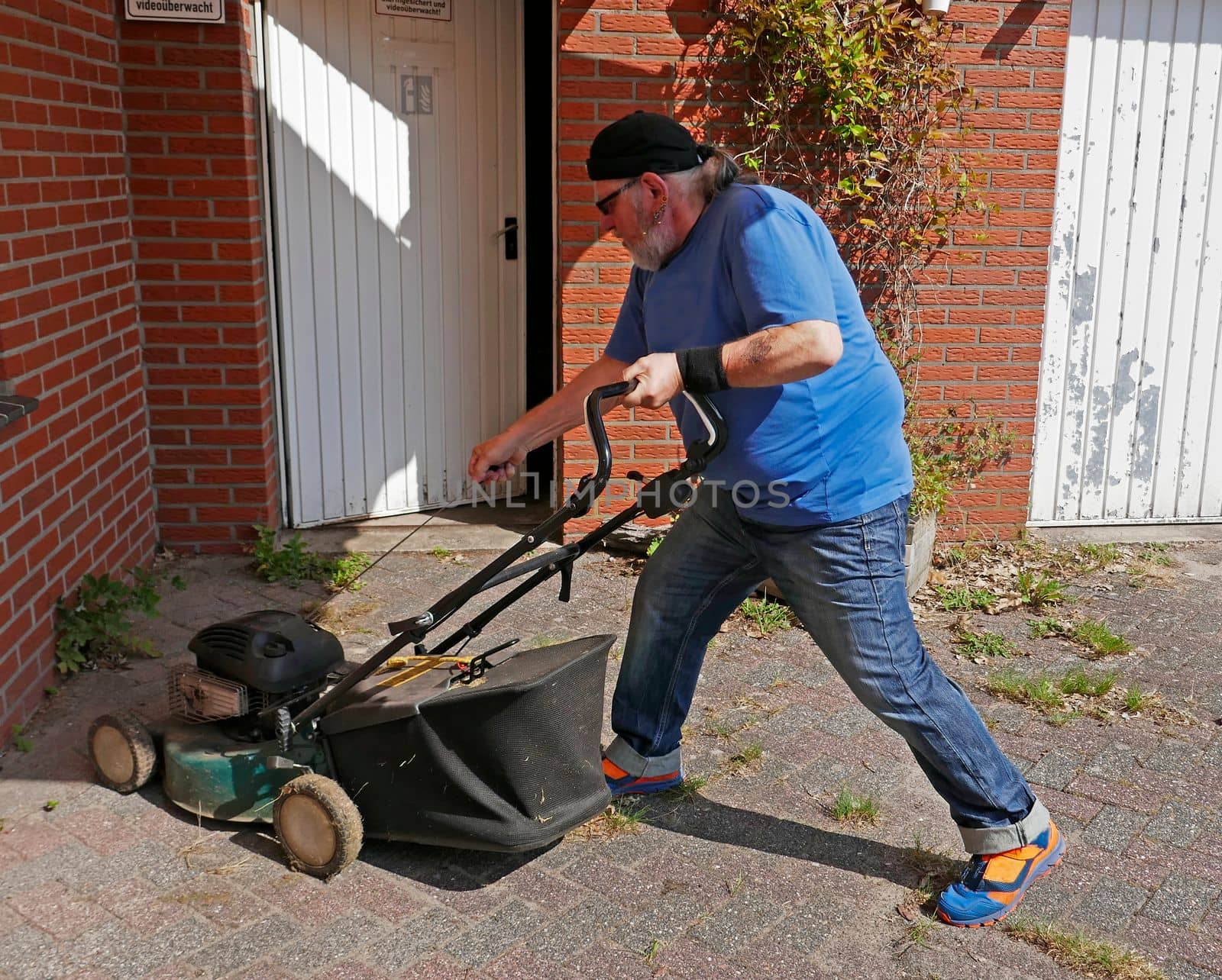 Active elderly man energetically starts his gas lawnmower. He pulls the starter cord