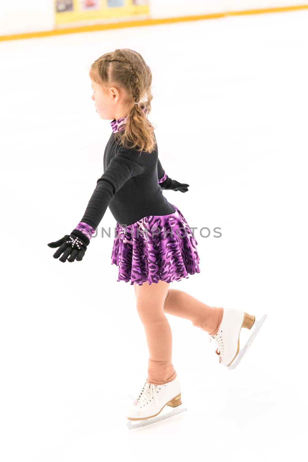 Little girl practicing figure skating on indoor ice skating rink.