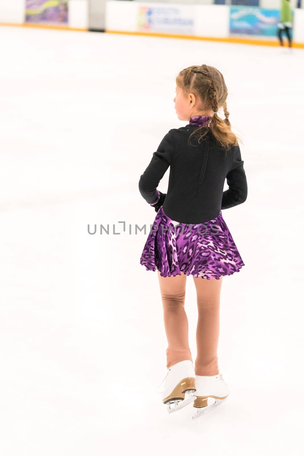 Little girl practicing figure skating on indoor ice skating rink.