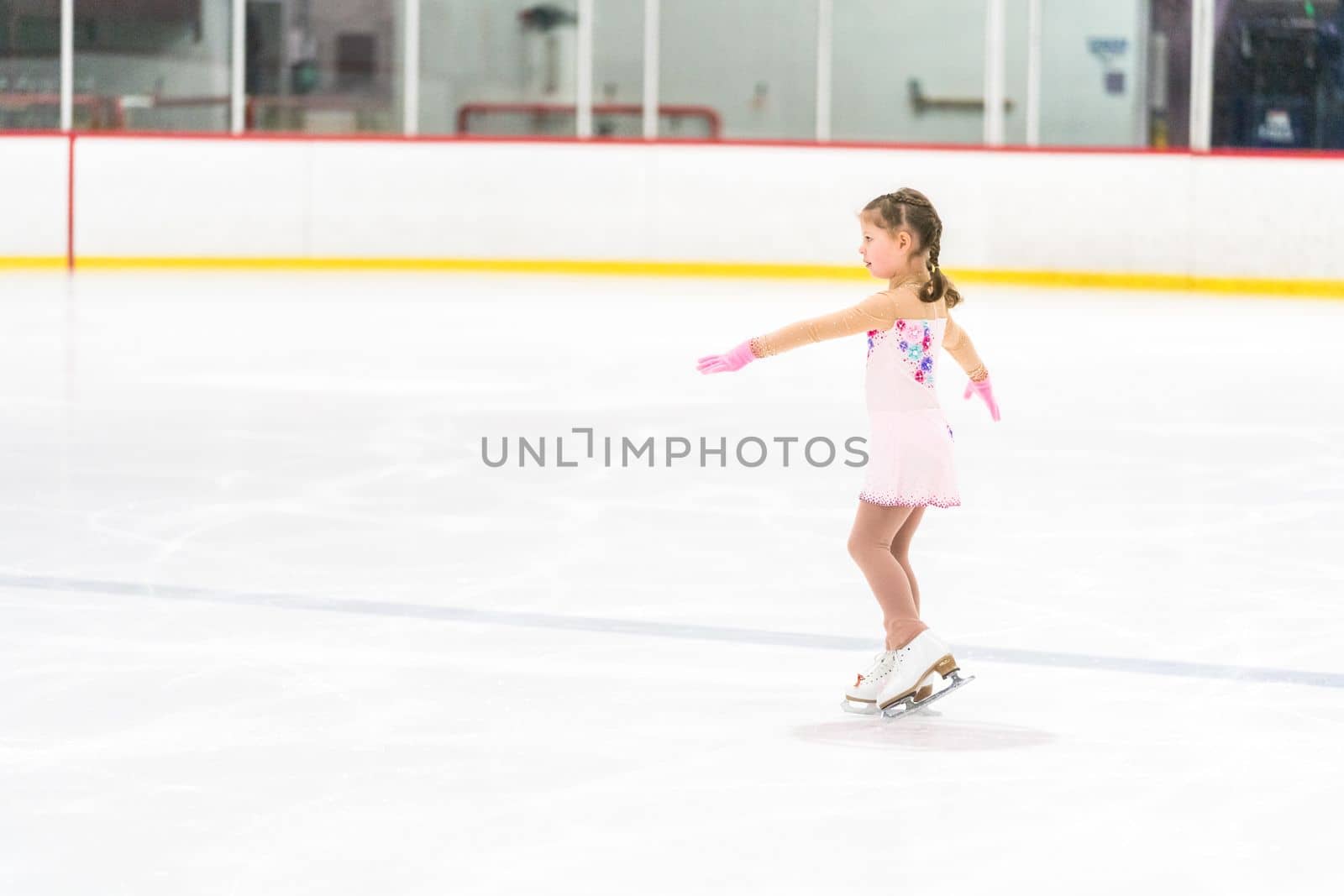 Little girl practicing figure skating on an indoor ice skating rink.