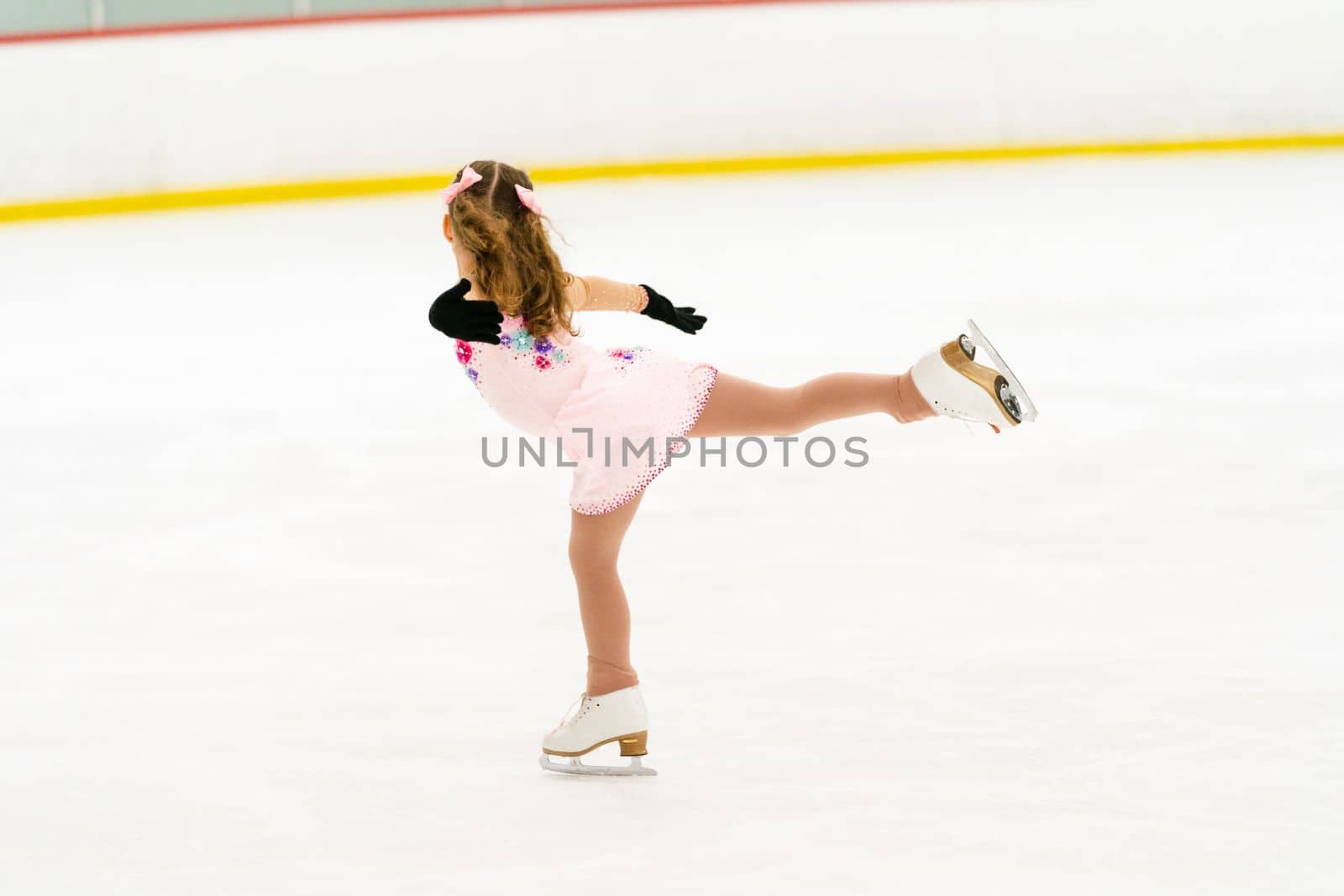 Little girl practicing figure skating on an indoor ice skating rink.