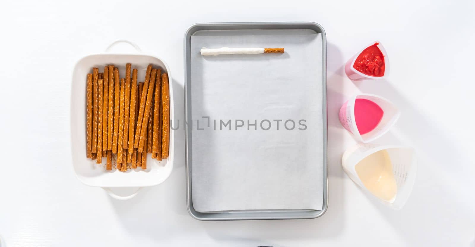 Flat lay. Dipping pretzels rods into silicone cup with melted chocolate to make chocolate-covered pretzel rods for Valentine's Day.