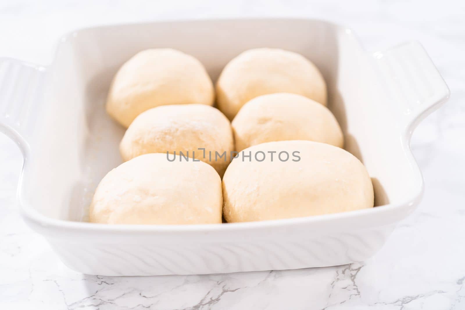 Rising dough in a white ceramic dish to prepare dinner rolls.