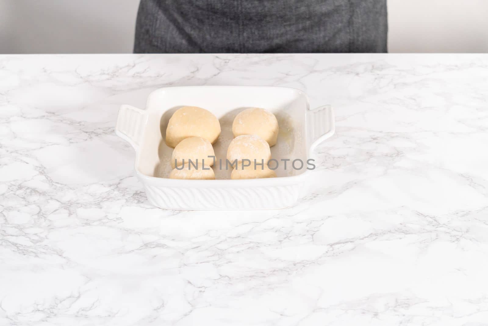 Rising dough in a white ceramic dish to prepare dinner rolls.
