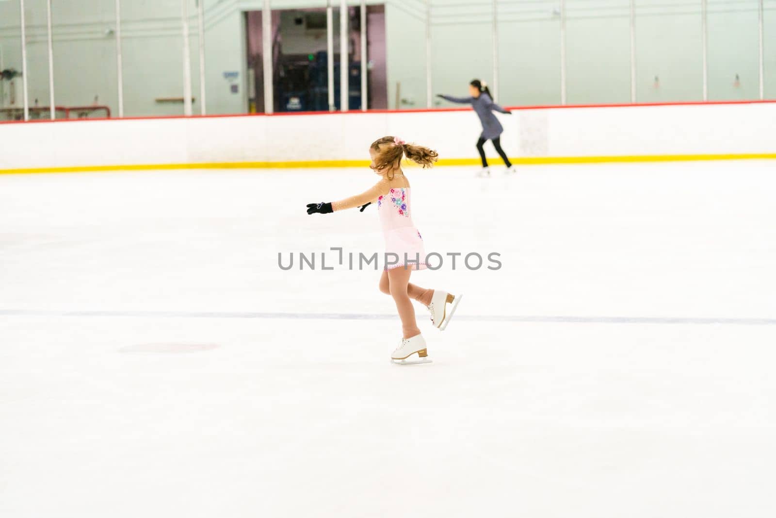 Little girl practicing figure skating on an indoor ice skating rink.