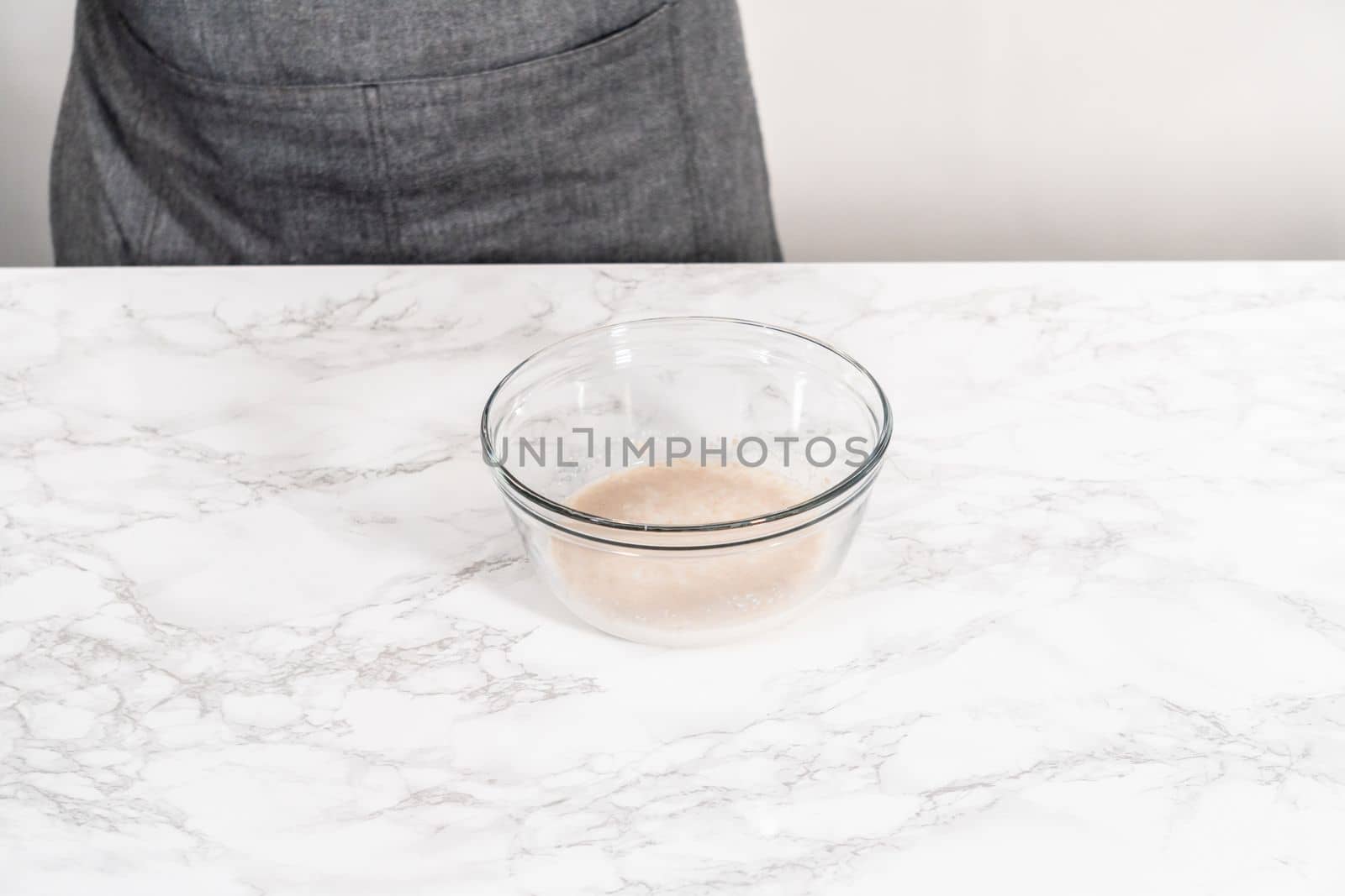 Activating dry yeast in a glass mixing bowl to prepare dinner rolls.