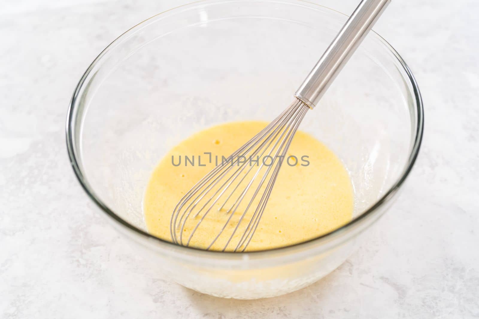 Mixing ingredients in a glass mixing bowl with a blending whisk to bake chocolate strawberry cupcakes.