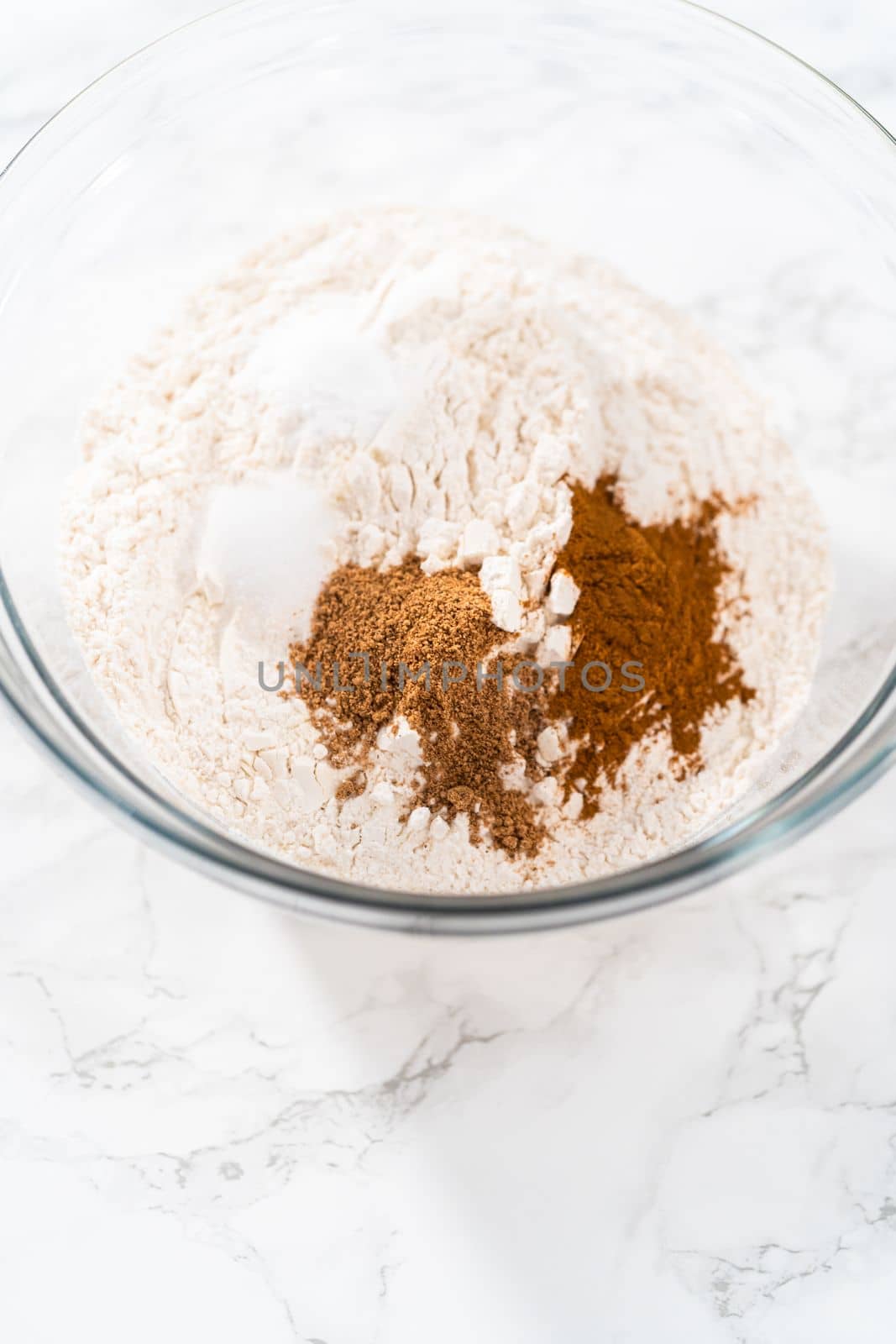 Mixing dry ingredients with a hand whisk in a large glass mixing bowl to bake eggnog bundt cake.