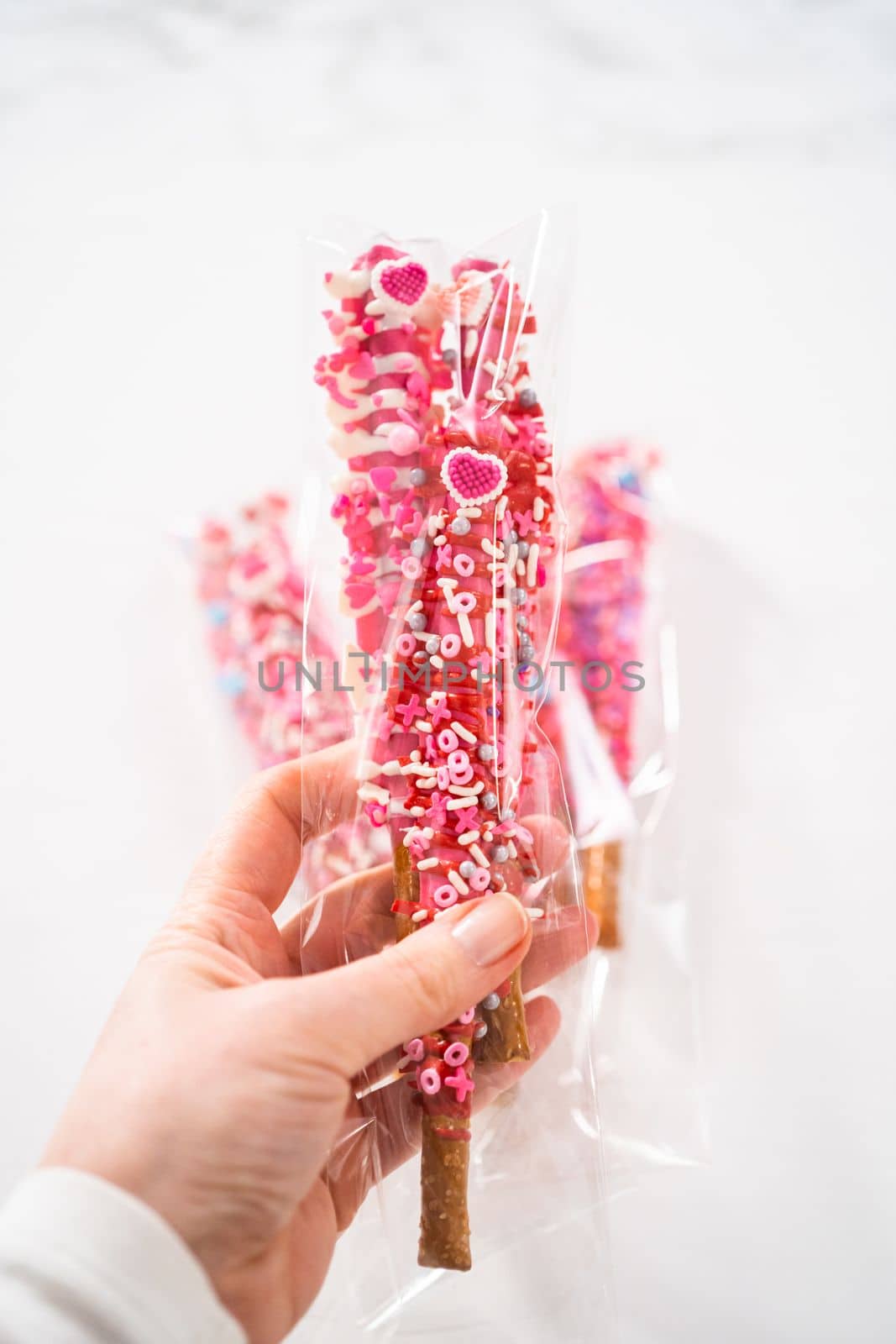 Chocolate-covered pretzel rods decorated with heart-shaped sprinkles for Valentine's Day packaged in a clear bags.