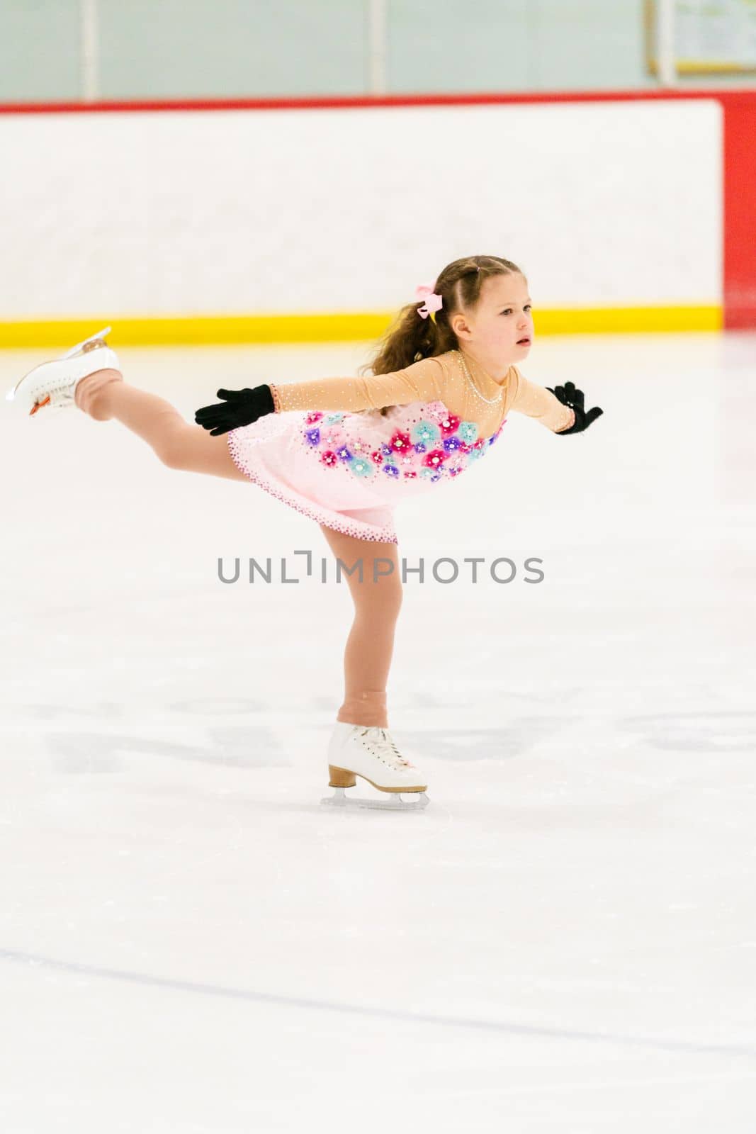 Little girl practicing figure skating on an indoor ice skating rink.