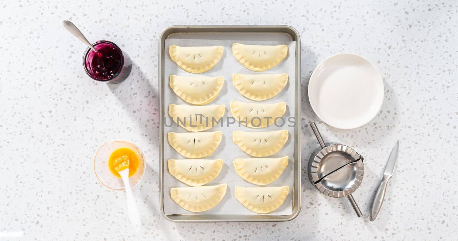 Flat lay. Brushing uncooked empanadas with blueberries with egg wash.