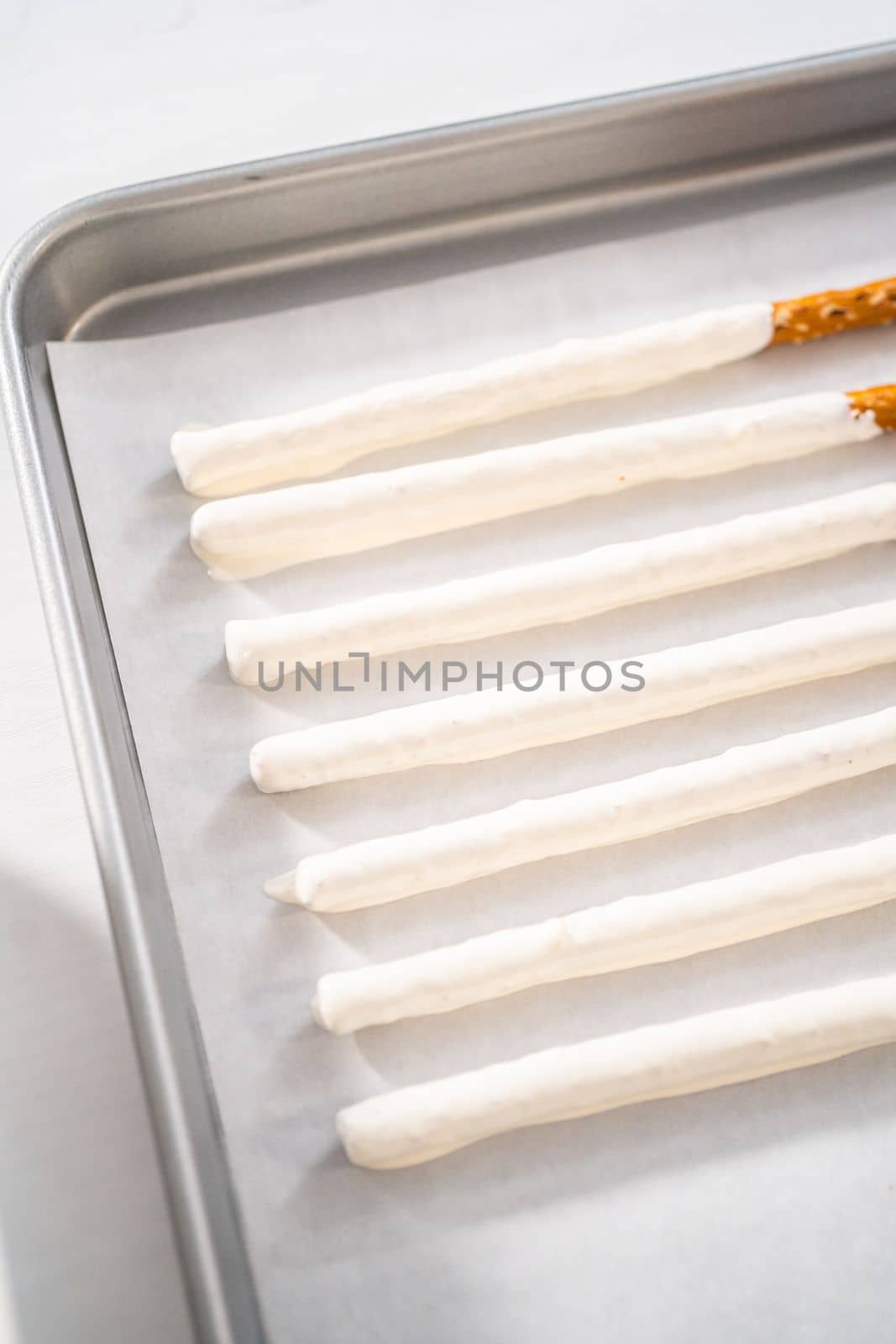 Dipping pretzels rods into silicone cup with melted chocolate to make chocolate-covered pretzel rods for Valentine's Day.