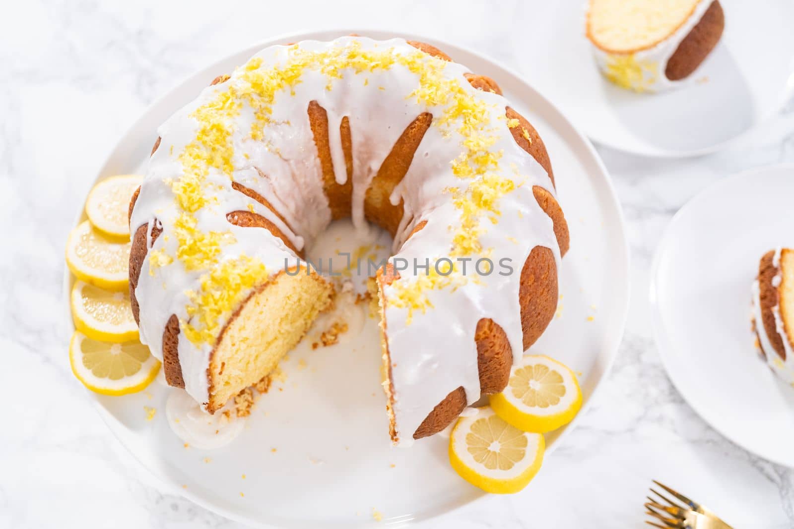 Sliced lemon bundt cake decorated with lemon zest on a cake stand.
