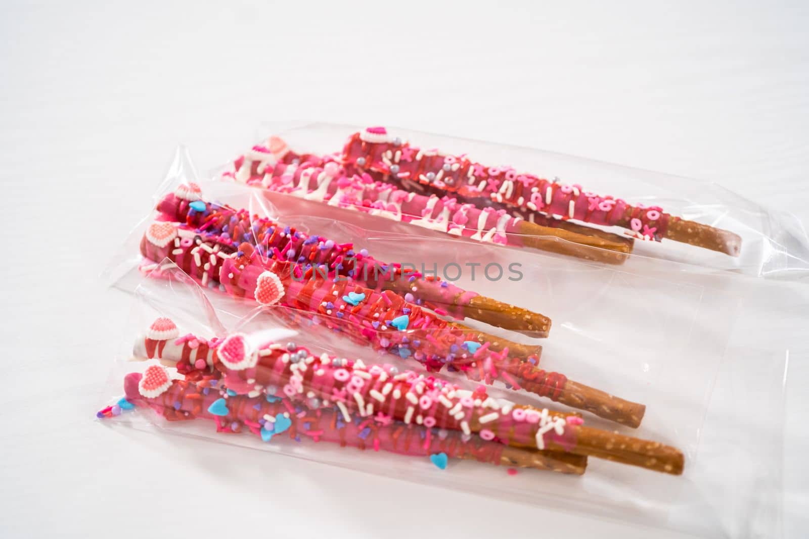 Chocolate-covered pretzel rods decorated with heart-shaped sprinkles for Valentine's Day packaged in a clear bags.