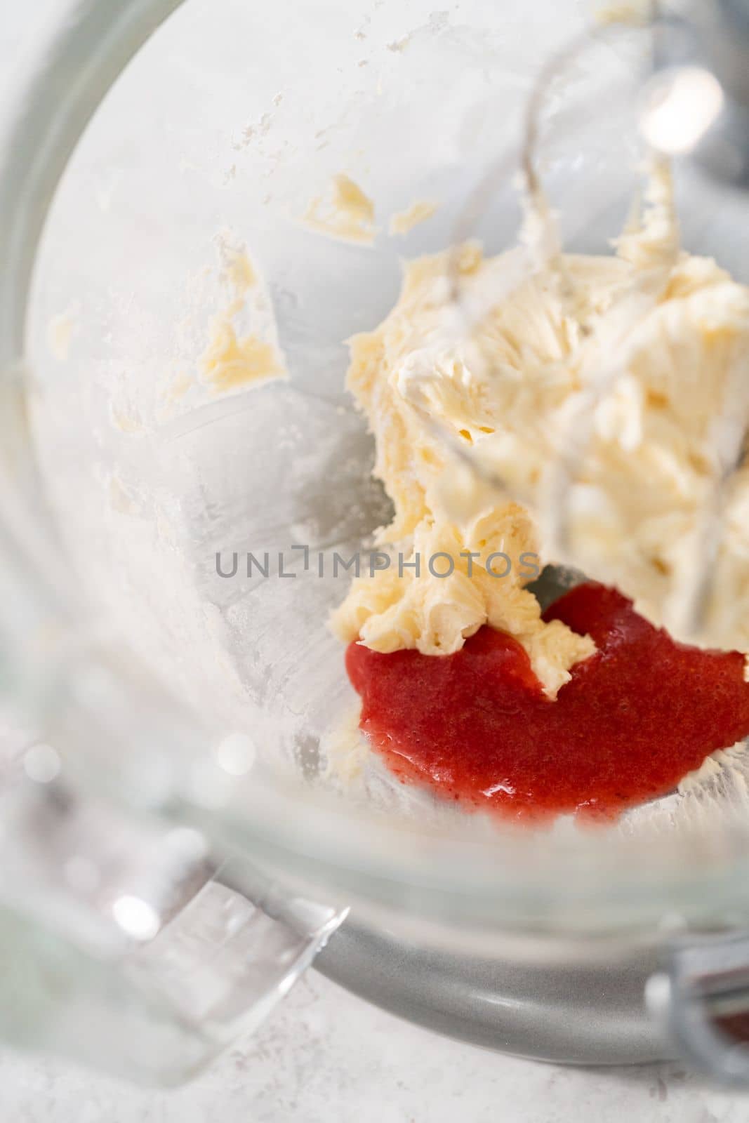 Whipping strawberry buttercream frosting in a stand-alone electric mixer with a whisk attachment.
