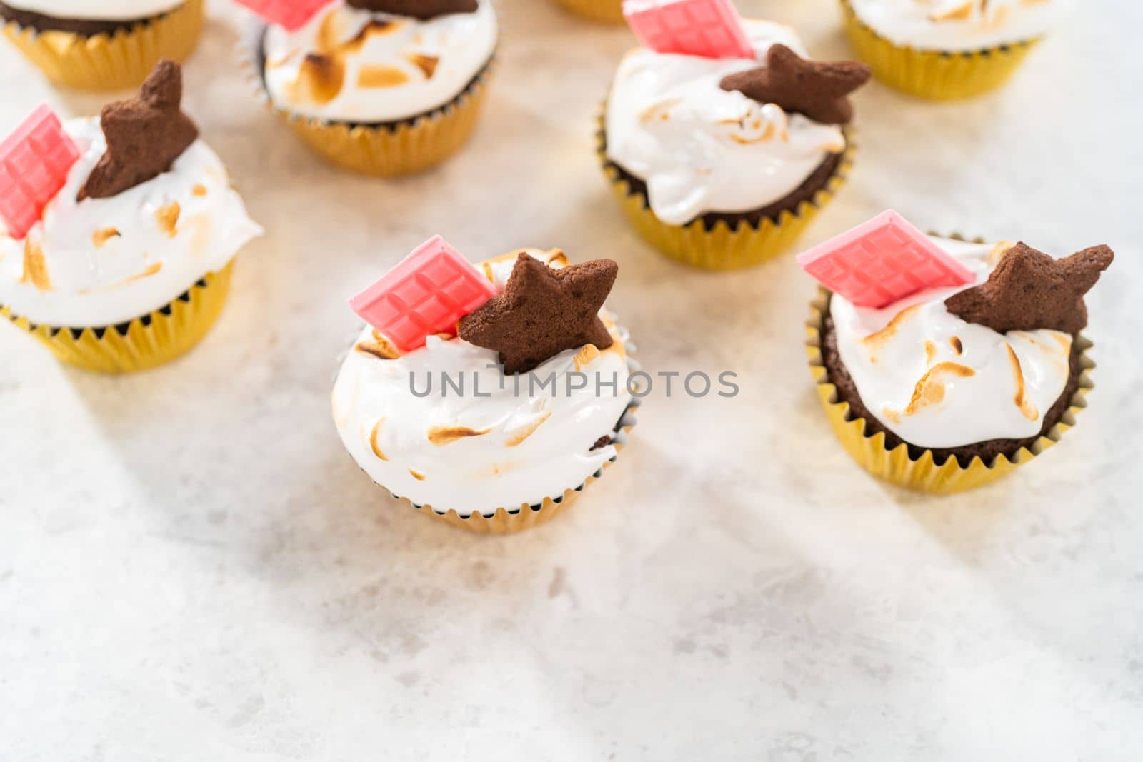 Gourmet s'mores cupcakes with meringue frosting and garnished with star-shaped chocolate graham cracker and a mini pink chocolate bar.