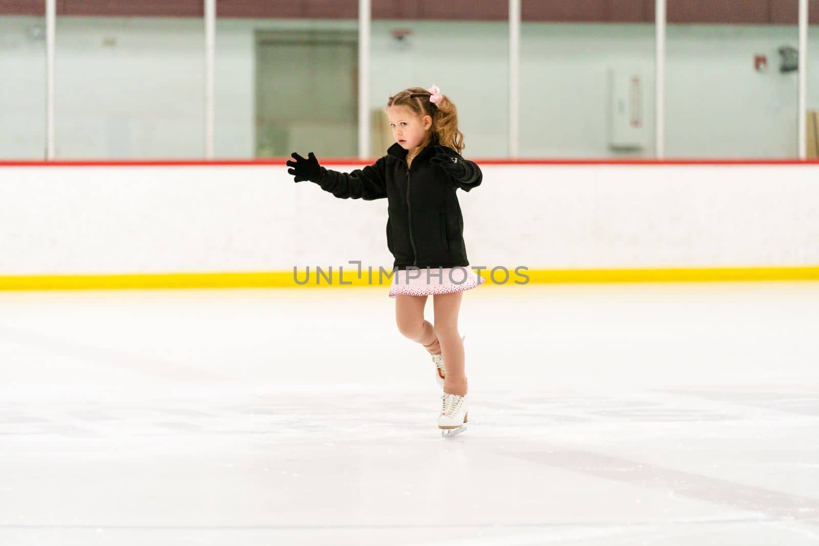 Little girl practicing figure skating on an indoor ice skating rink.