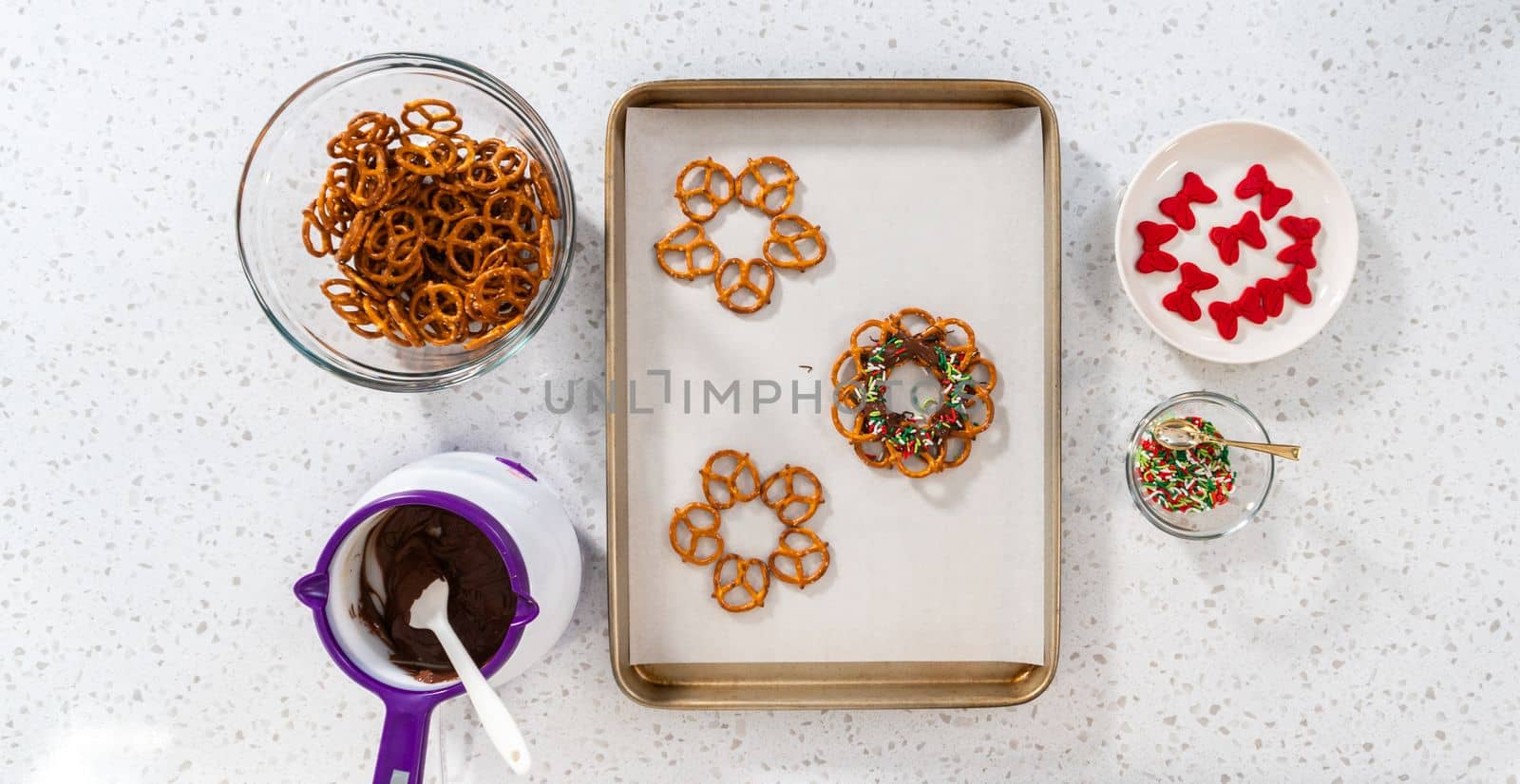 Flat lay. Dipping pretzels twists into melted chocolate to make a chocolate pretzel Christmas wreath.
