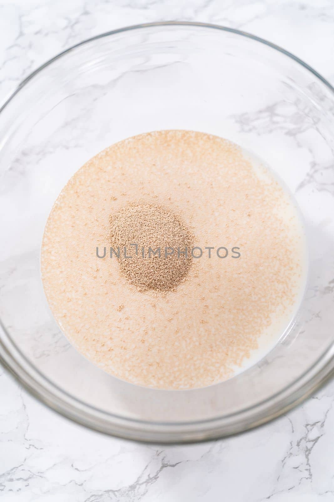 Activating dry yeast in a glass mixing bowl to prepare dinner rolls.
