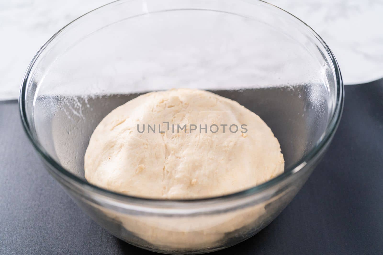 Rising dough in a glass mixing bowl to prepare dinner rolls.