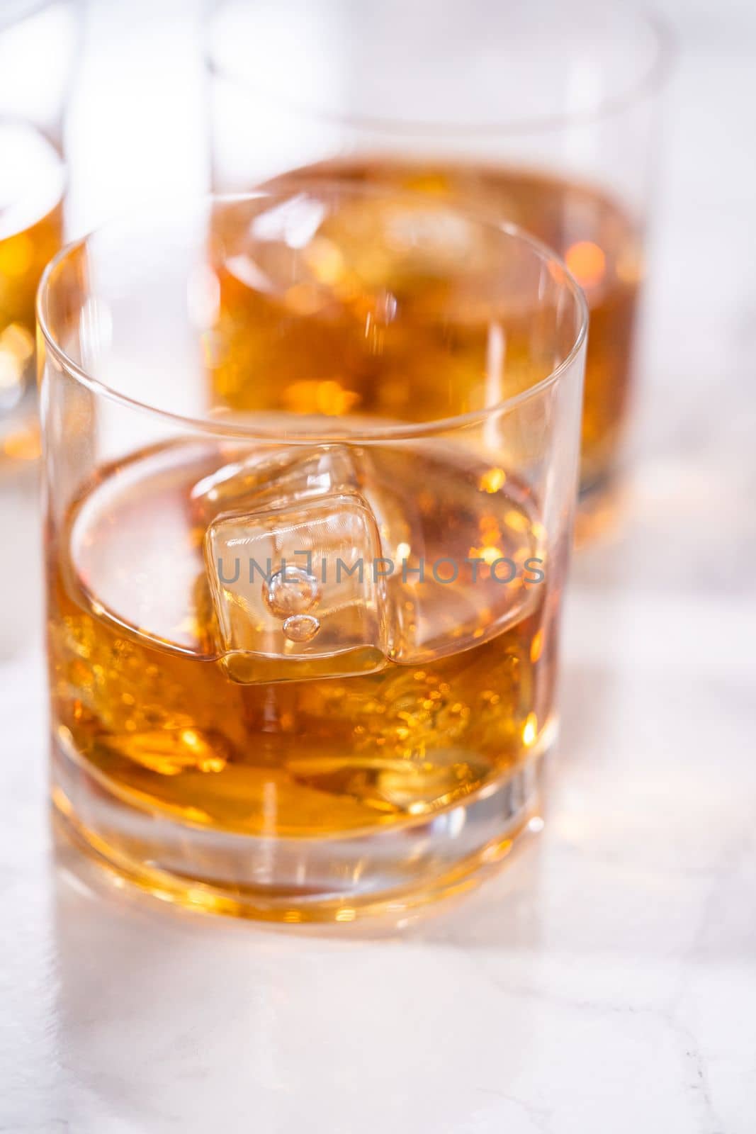 Scotch on the rocks in whiskey glass on a white marble surface.