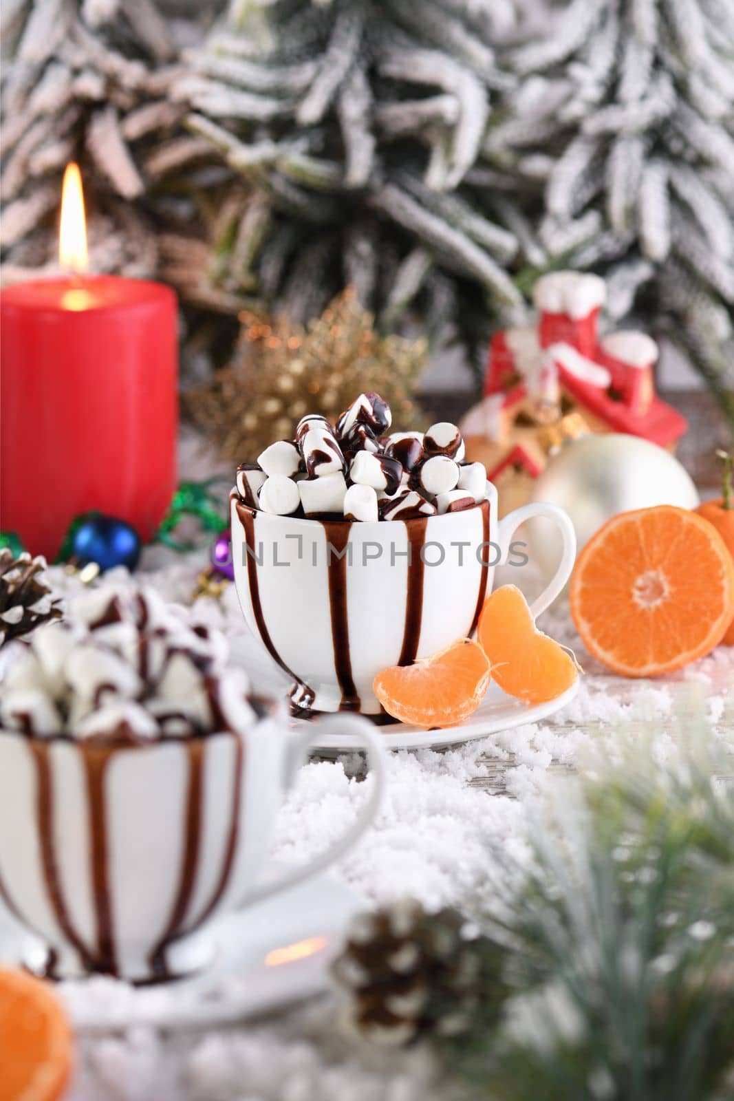 Hot chocolate with marshmallows in a white ceramic mug, with tangerines on a snowy table. The concept of a cozy holiday for Christmas and New Year.