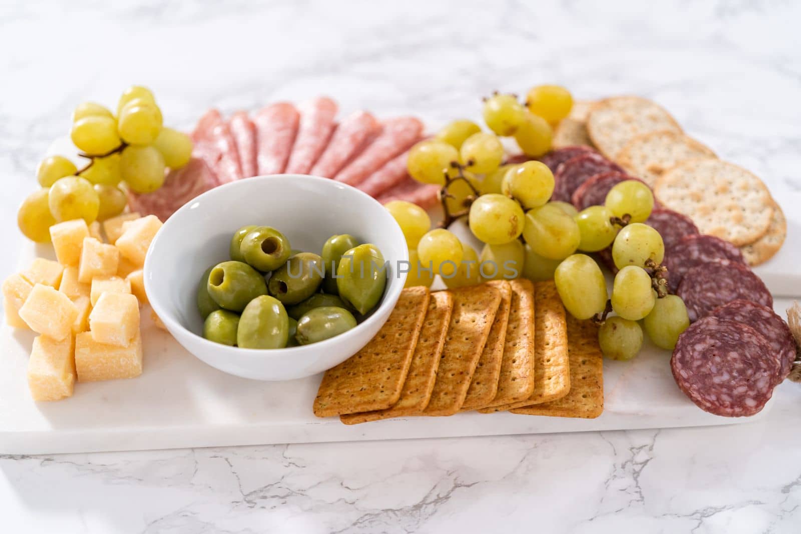 Cheese, meat, and crackers appetizer board on a marble surface.