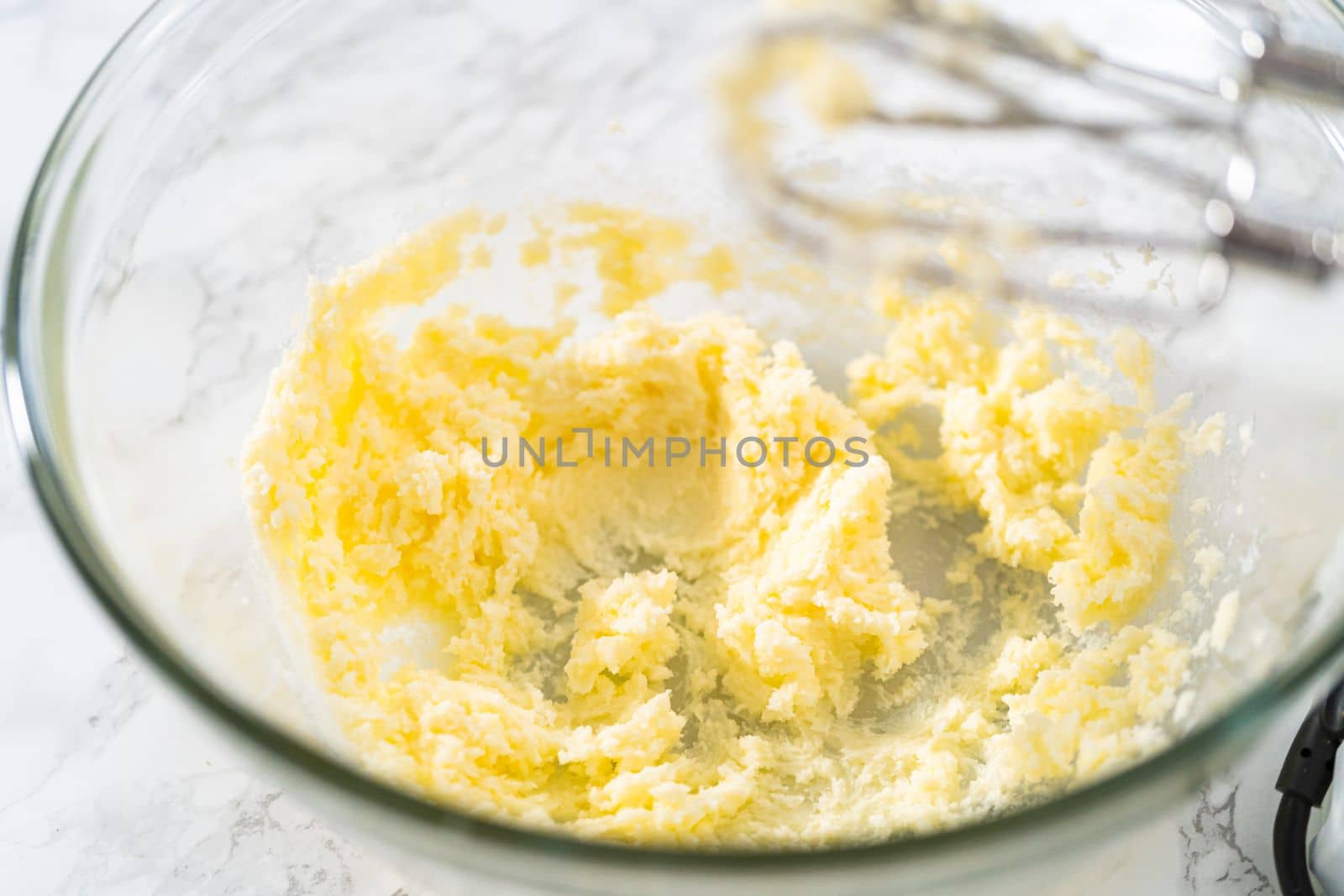 Mixing ingredients with a hand mixer in a large mixing bowl to bake mini vanilla cupcakes with ombre pink buttercream frosting.