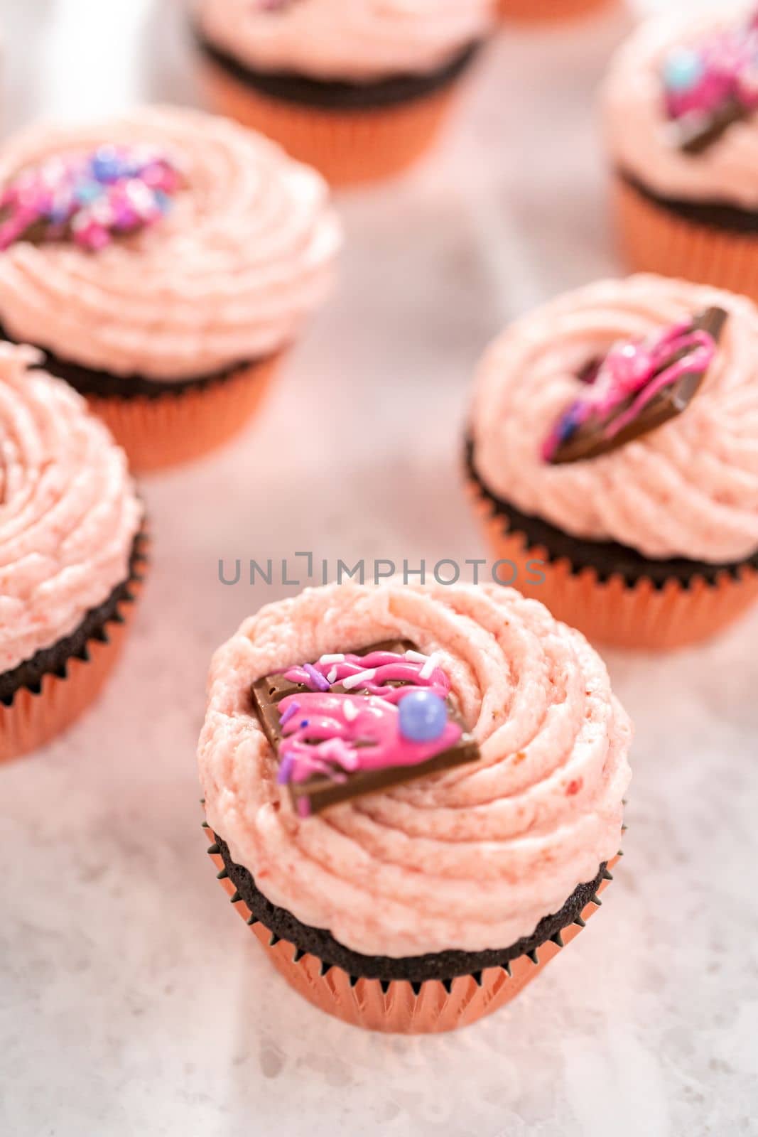 Freshly baked chocolate strawberry cupcakes garnished with gourmet mini pink chocolates.