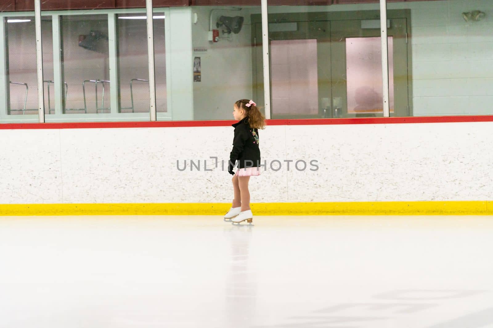 Little girl practicing figure skating on an indoor ice skating rink.