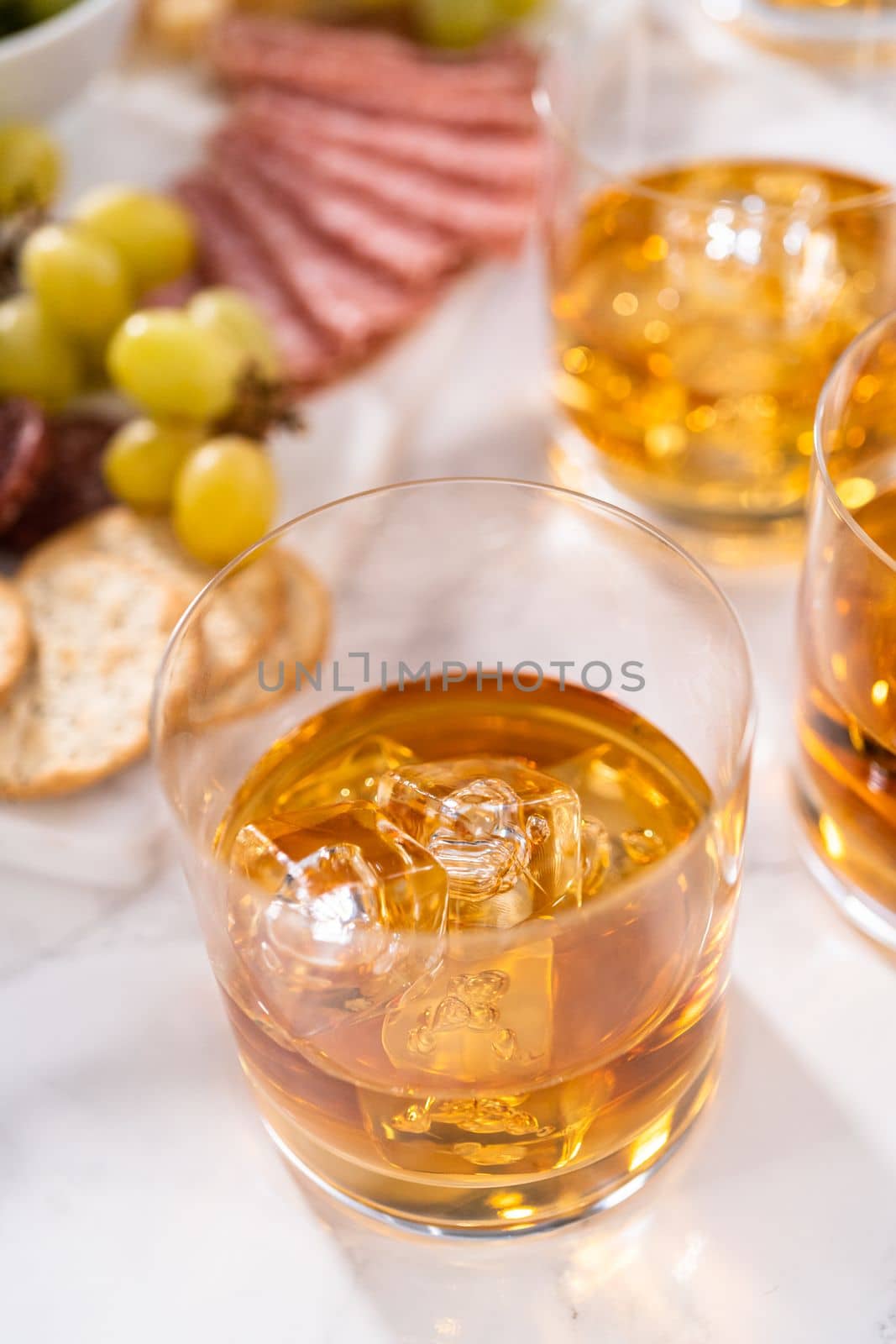Scotch on the rocks in whiskey glass on a white marble surface.