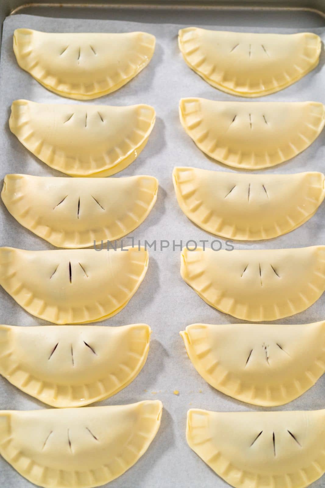 Brushing uncooked empanadas with blueberries with egg wash.