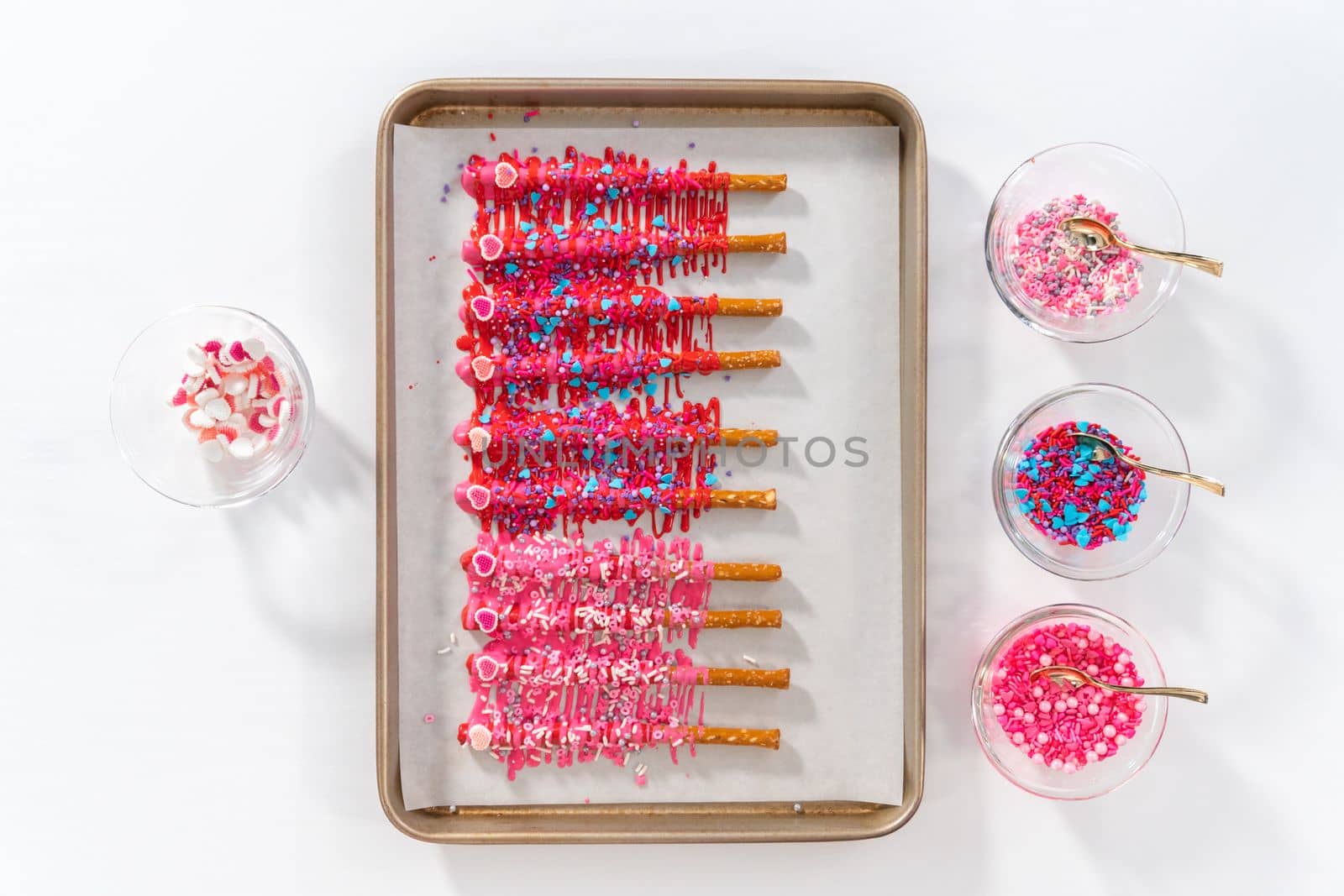 Flat lay. Drizzling melted chocolate over chocolate-dipped pretzels rods and decorating with sprinkles to make chocolate-covered pretzel rods for Valentine's Day.
