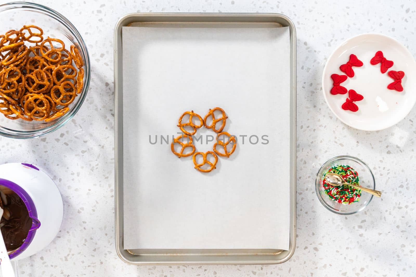 Flat lay. Dipping pretzels twists into melted chocolate to make a chocolate pretzel Christmas wreath.