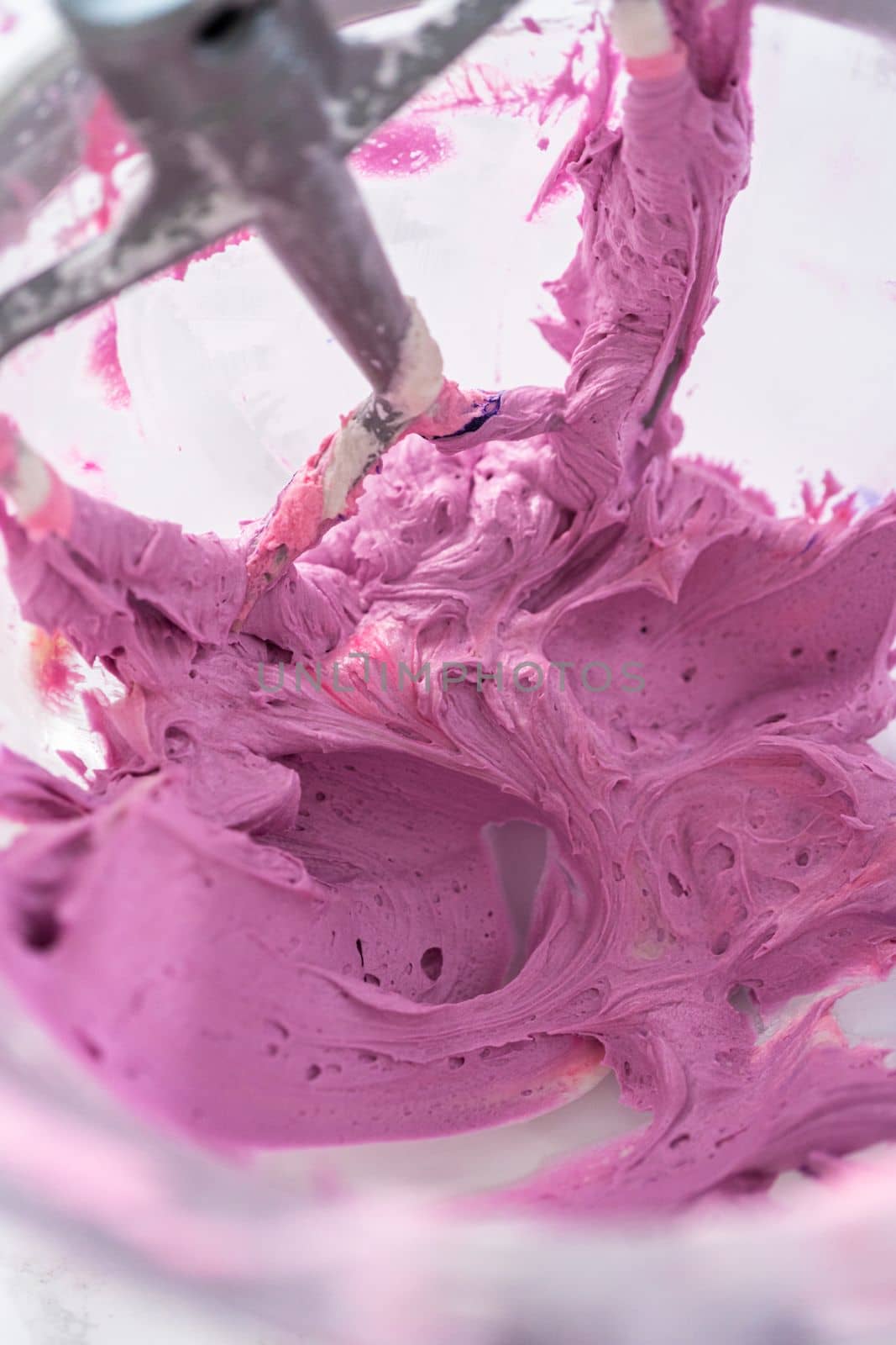 Mixing ingredients in kitchen electric mixer to make ombre pink buttercream frosting.