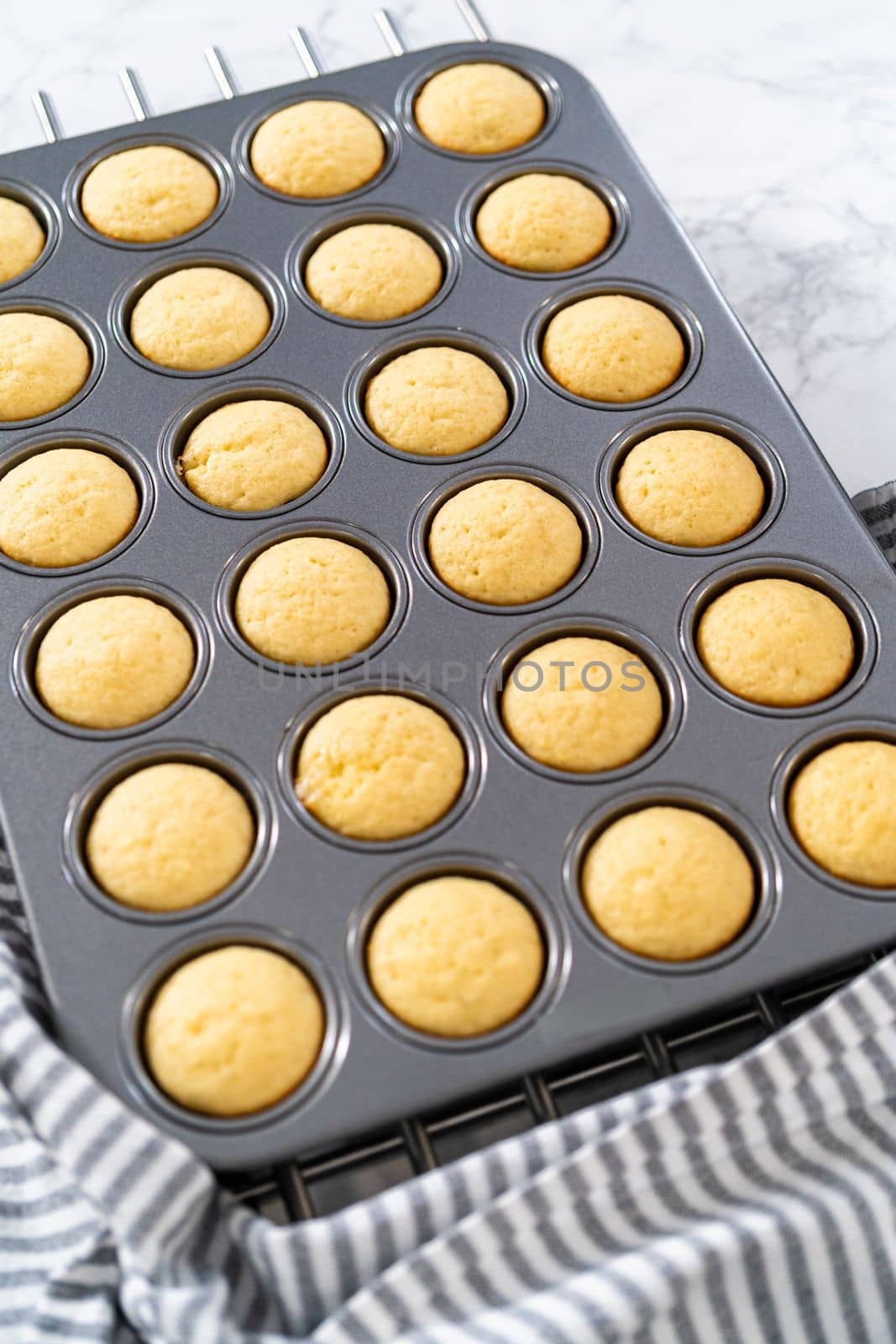 Cooling freshly baked mini vanilla cupcakes on a kitchen counter.