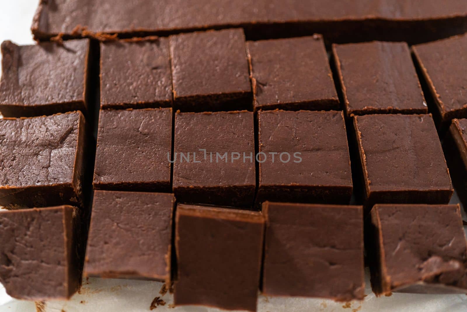 Cutting plain homemade fudge into small pieces on a white cutting board.