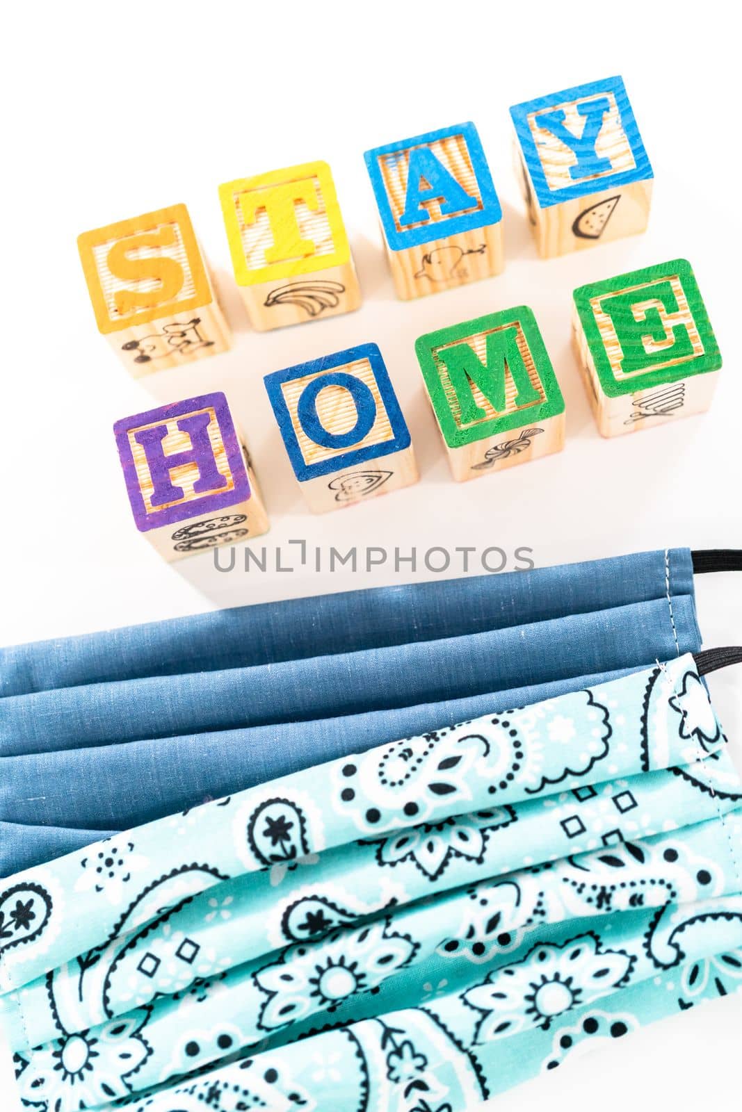STAY HOME sign out of kids' alphabet blocks with homemade face masks on a white background.