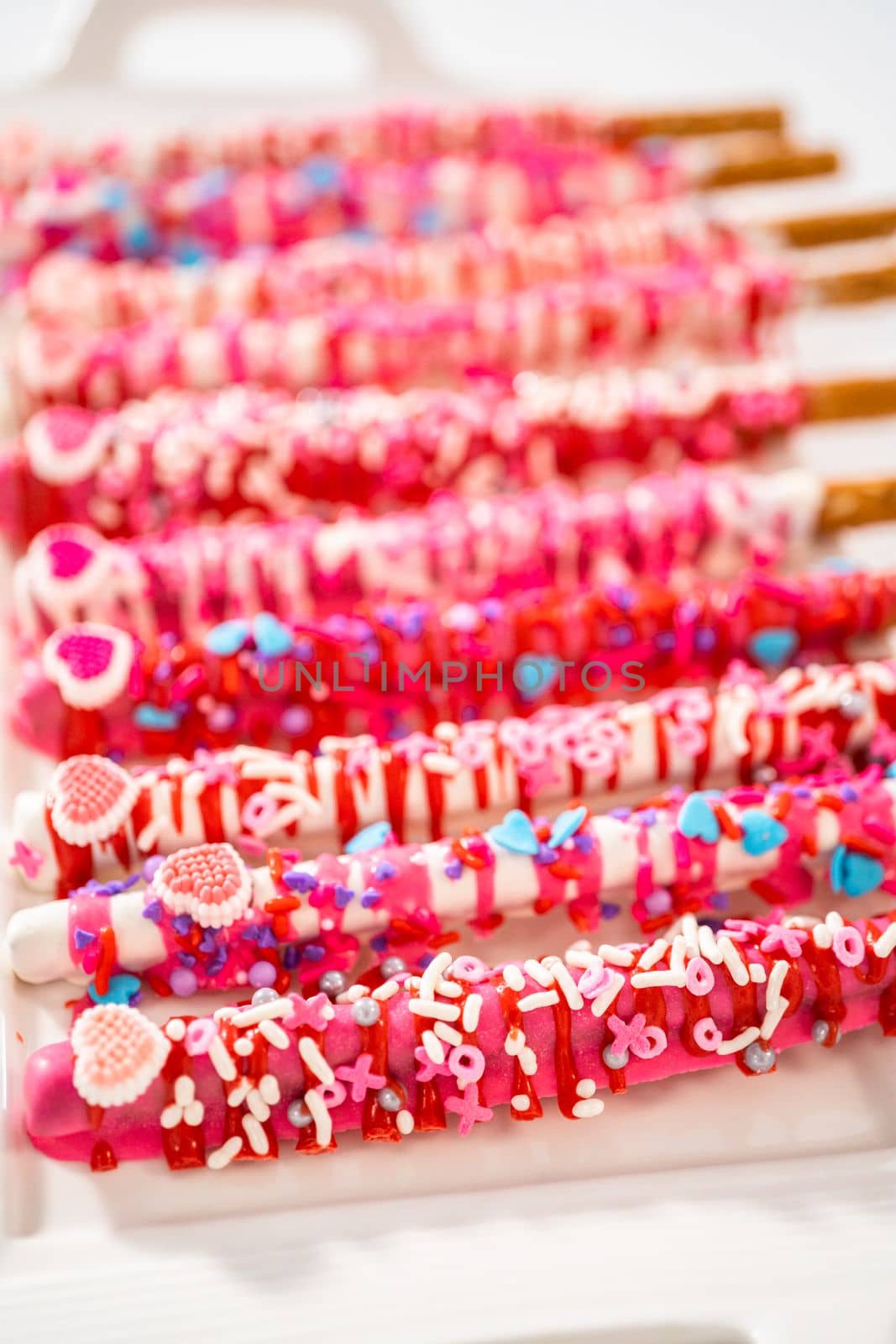 Chocolate-covered pretzel rods decorated with heart-shaped sprinkles for Valentine's Day.