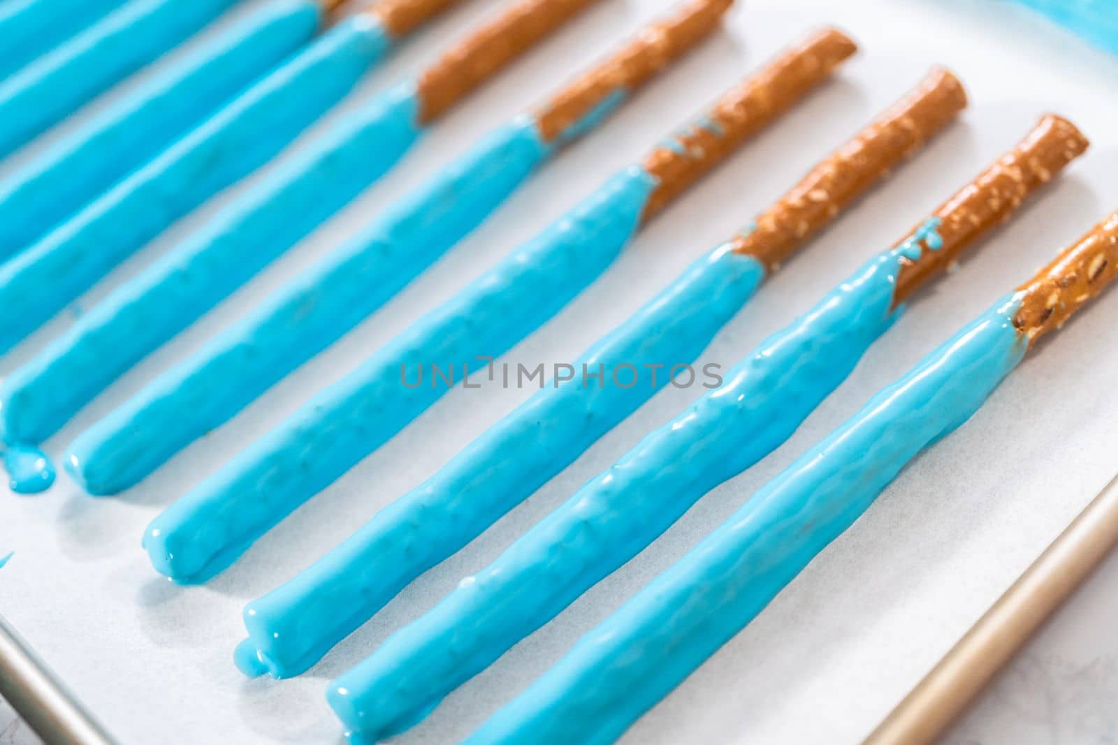 Dipped in chocolate pretzel rods drying on a baking sheet lined with parchment paper.
