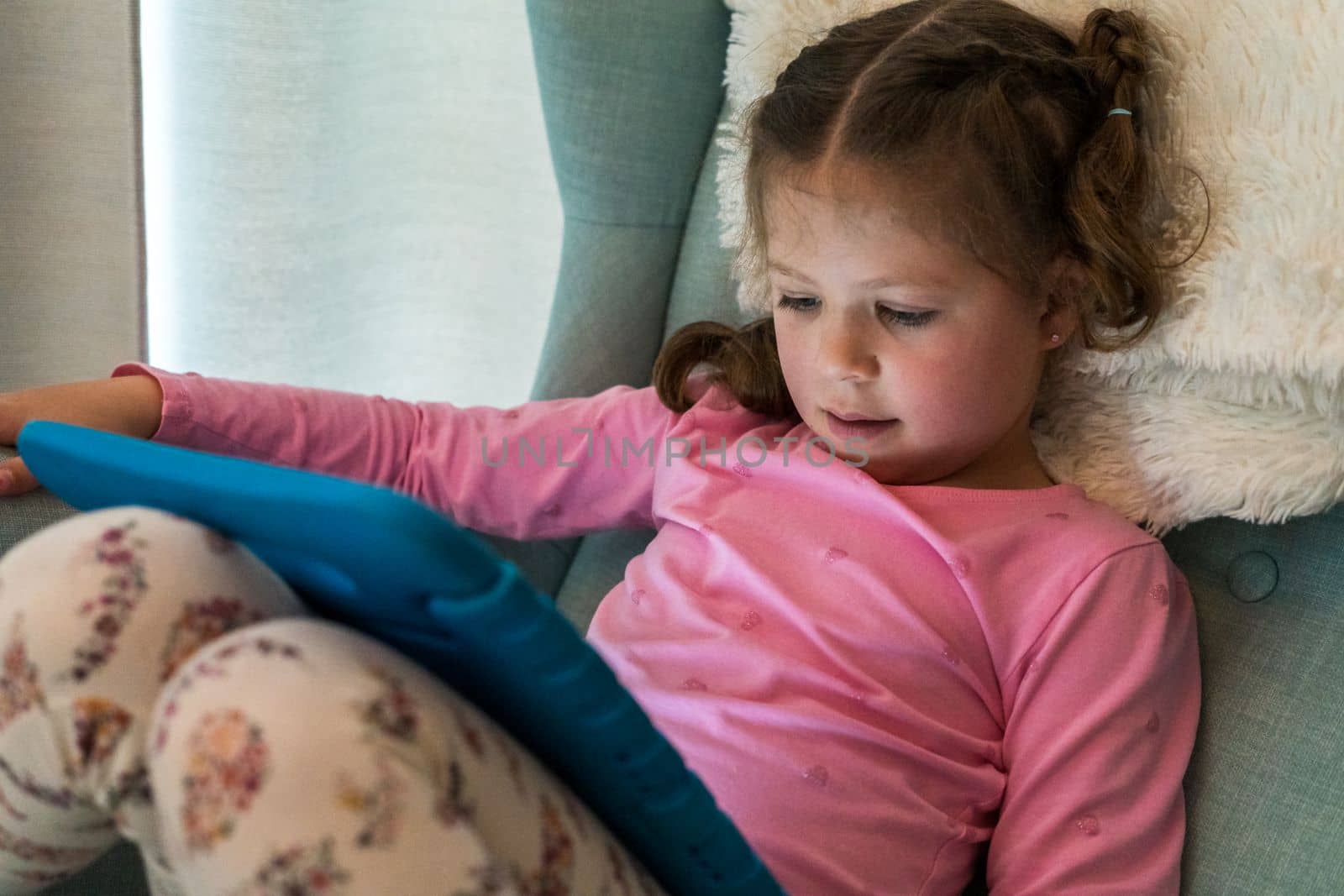 Little girl reading books on her tablet at homeschool.