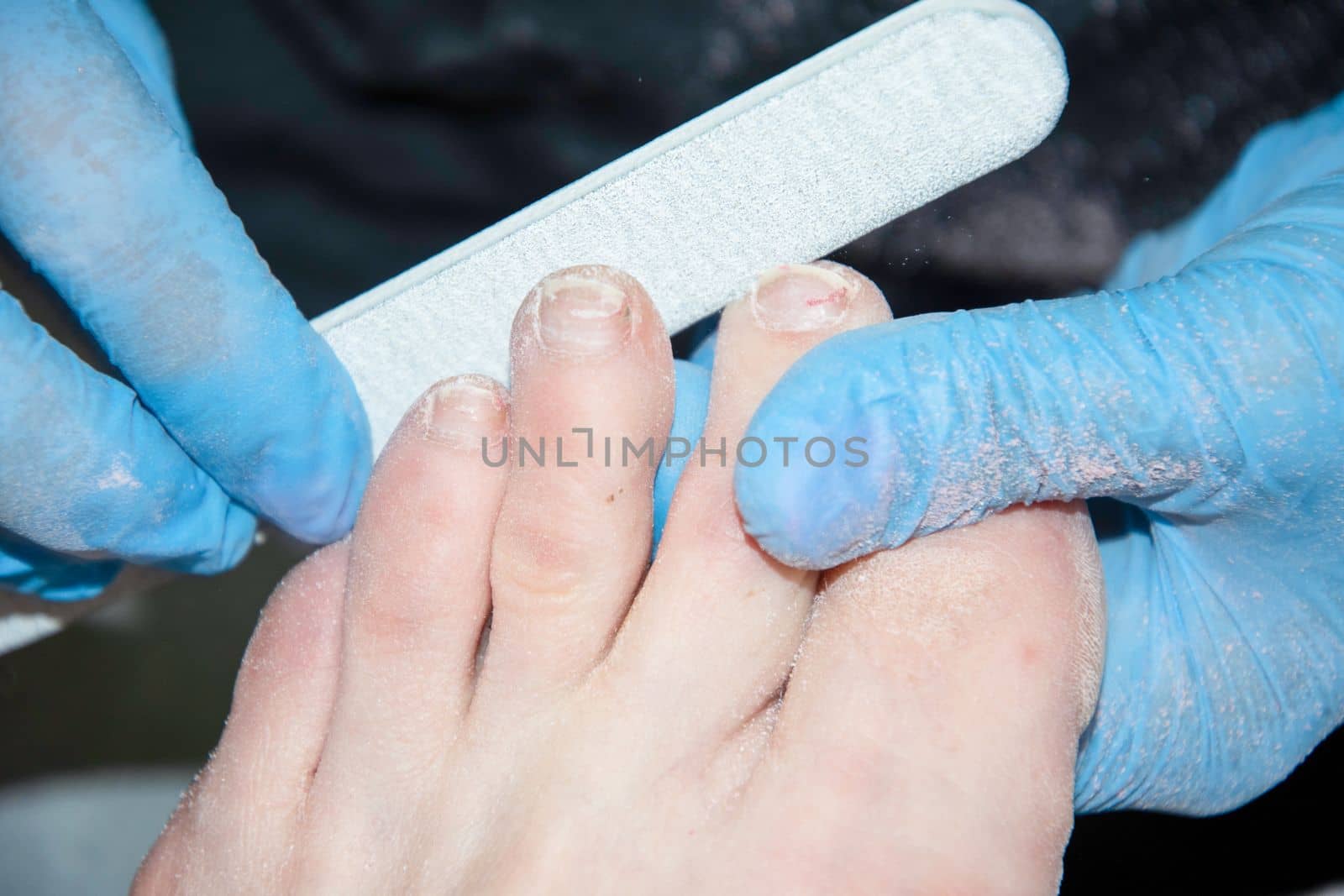 The pedicure master grinds the toenails of clients with a nail file, polishes polishing the nail plate with a buff, High quality photo