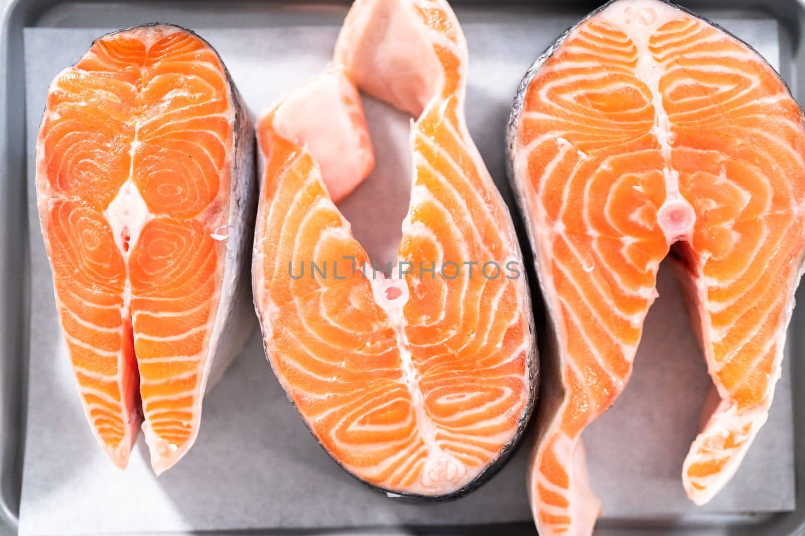 Farm-raised salmon steaks on a cooking tray with a parchment paper.