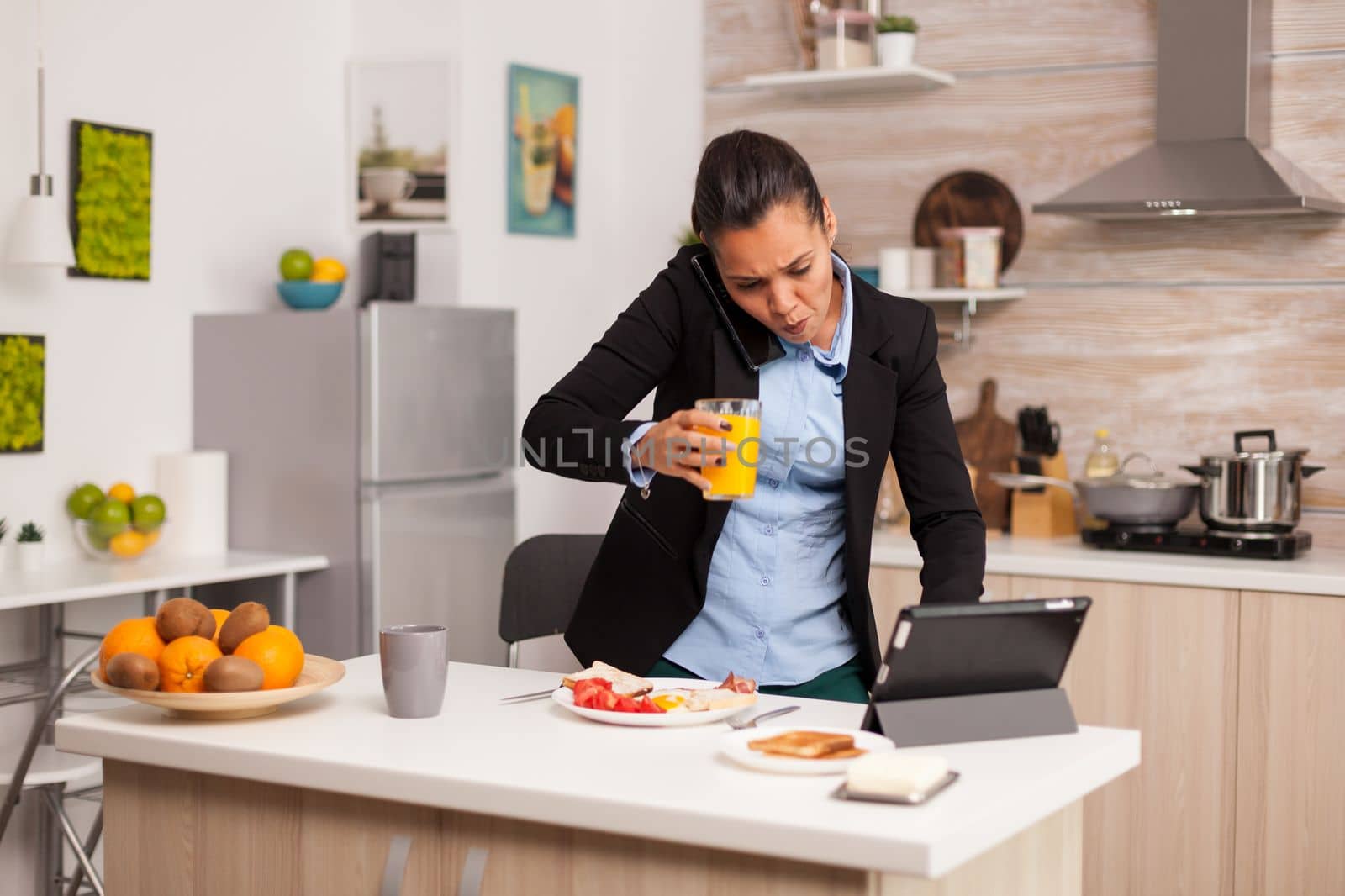 Hurried freelancer having a video call in the morning during breakfast. Concentrated business woman in the morning multitasking in the kitchen before going to the office, stressful way of life, career and goals to meet.