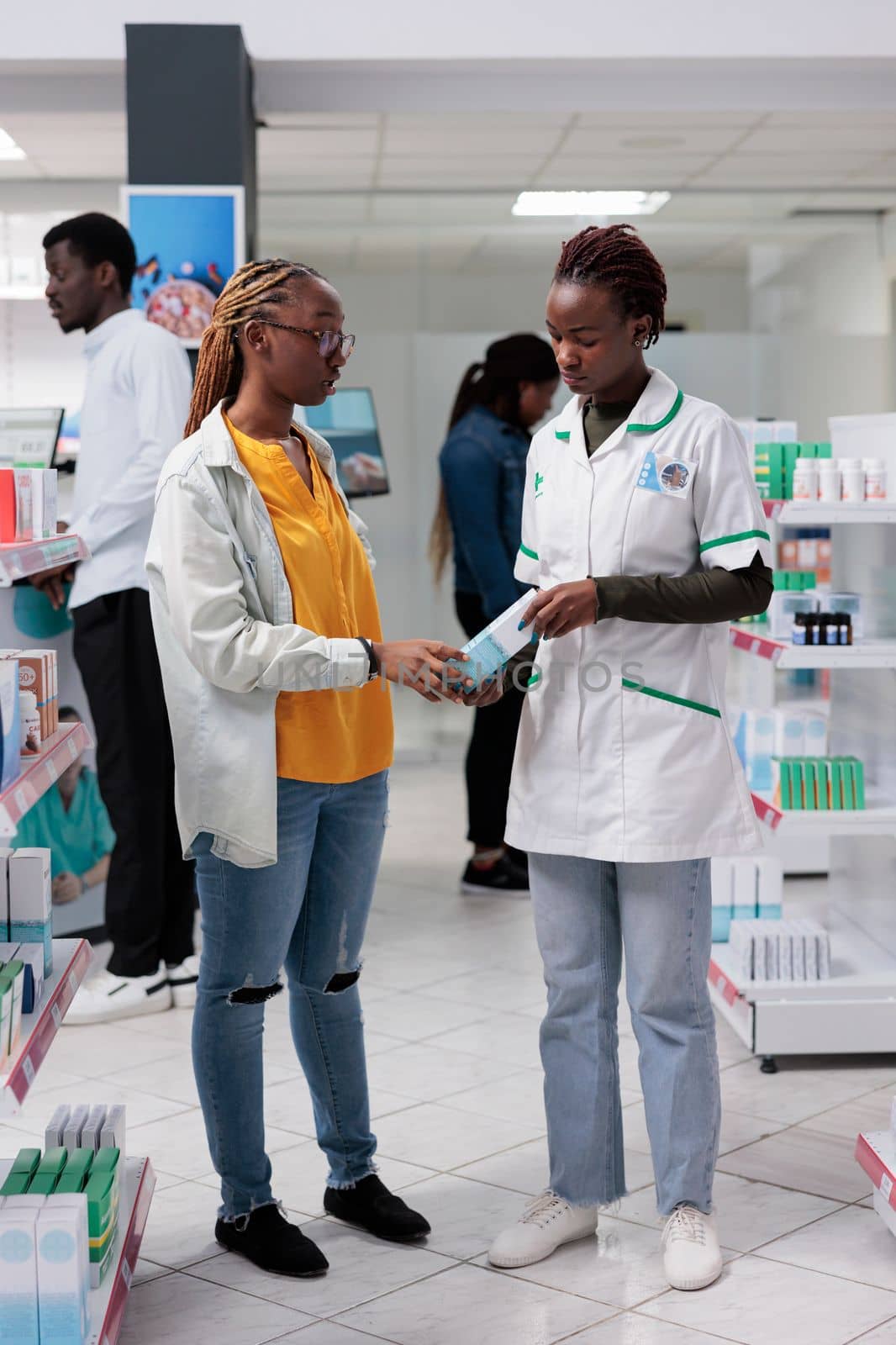 African american pharmacist helping woman choosing medications in drugstore by DCStudio